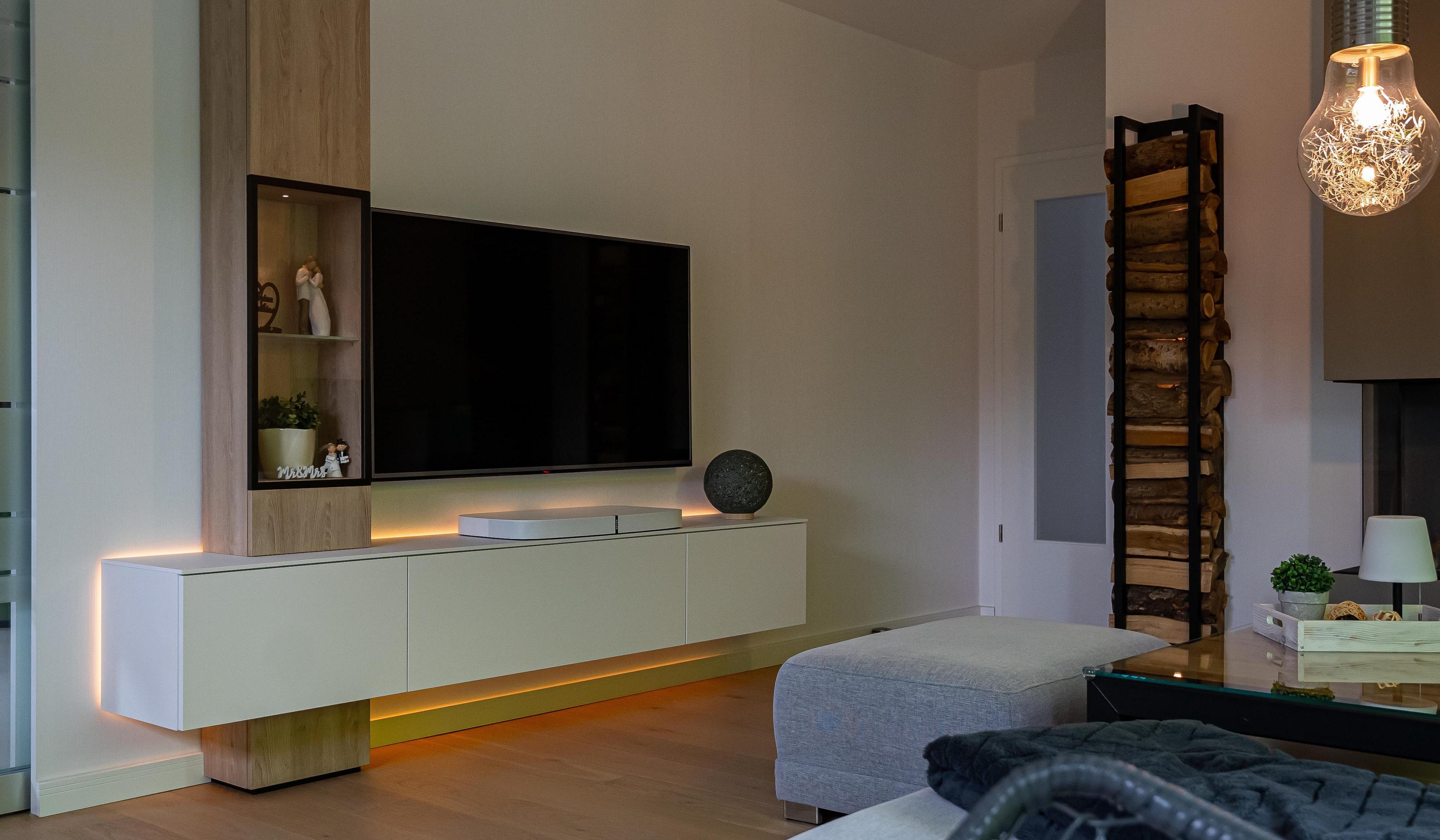 Moderne Wohnwand mit TV, weißem Lowboard, Holzdekor und indirekter LED-Beleuchtung