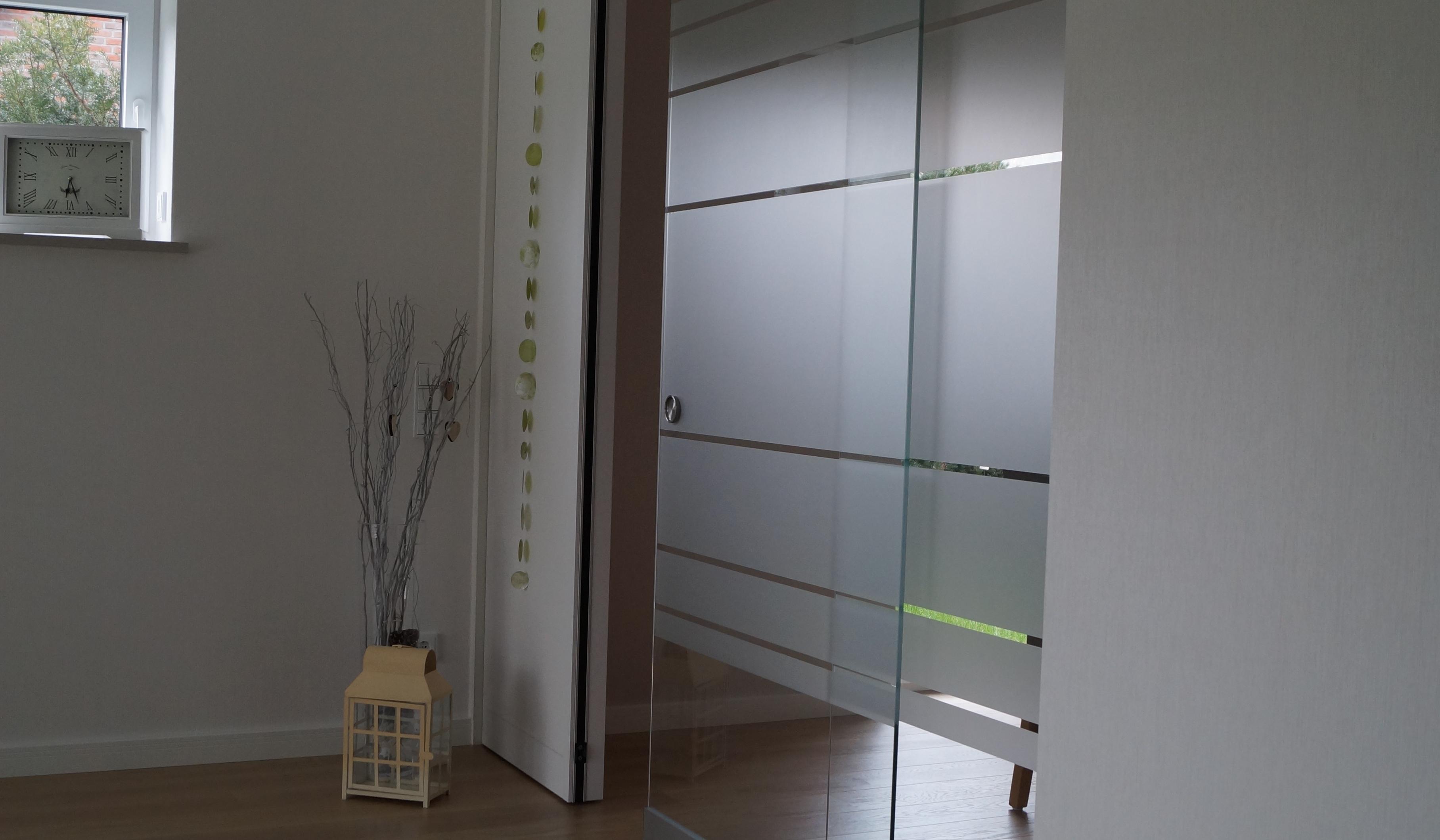 Große Glasschiebetür mit satinierten Streifen als moderner Raumteiler im hellen Wohnbereich