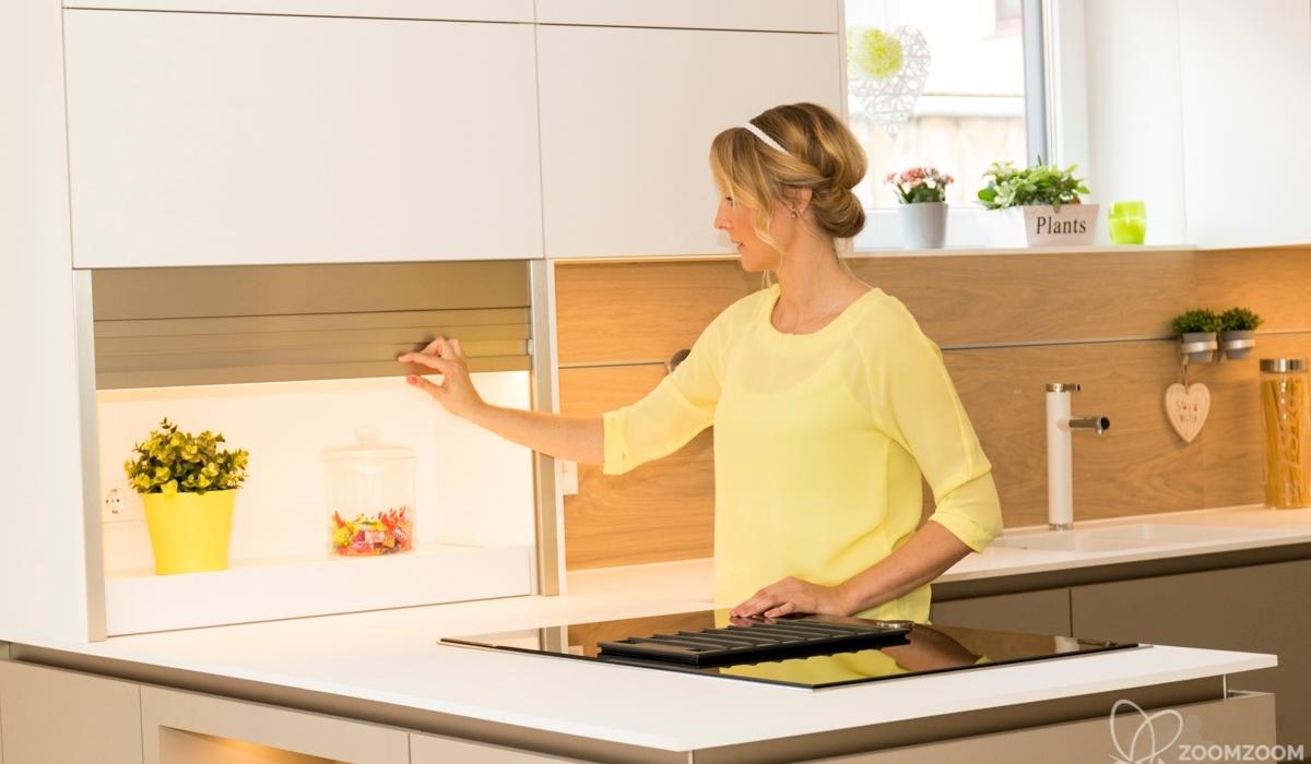 Moderne weiße Küche mit Kochinsel und geöffnetem Rollladenschrank für zusätzlichen Stauraum