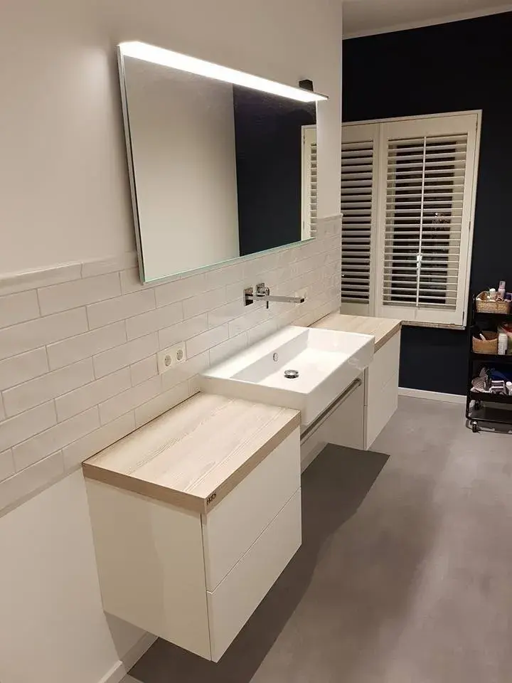 Modernes Badezimmer mit weißen grifflosen Badmöbeln, Aufsatzwaschbecken, Holzablage und beleuchtetem Spiegel