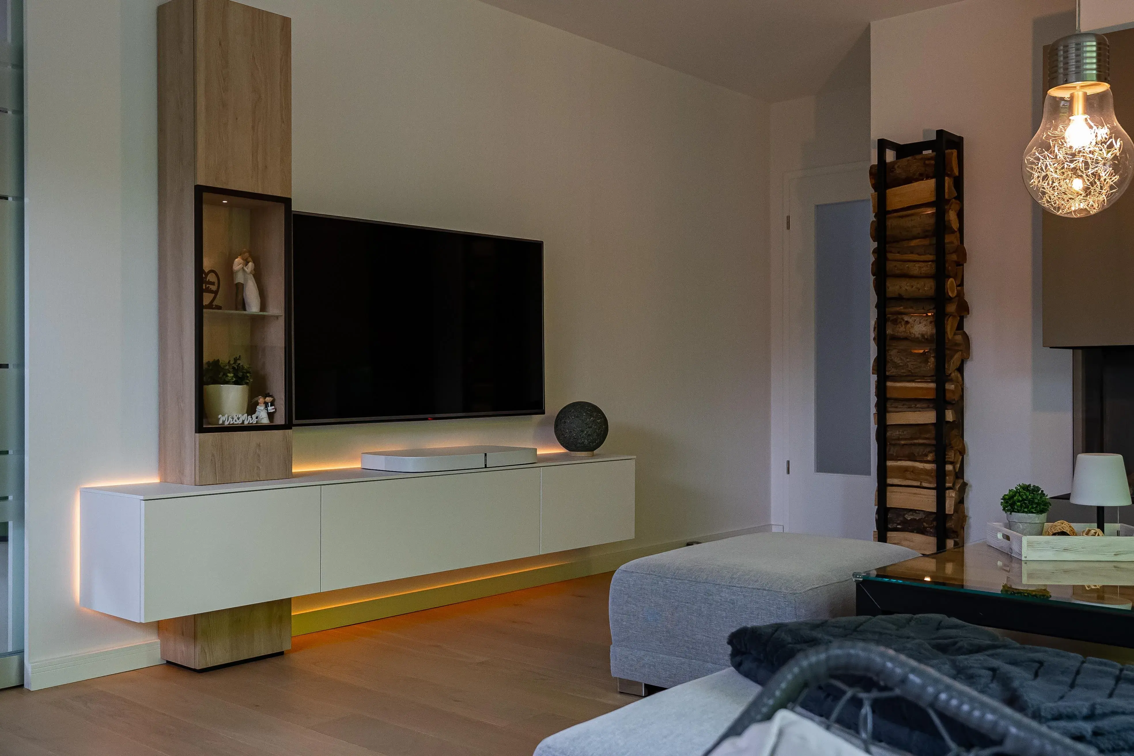 Moderne Wohnwand mit TV, weißem Lowboard, Holzdekor und indirekter LED-Beleuchtung