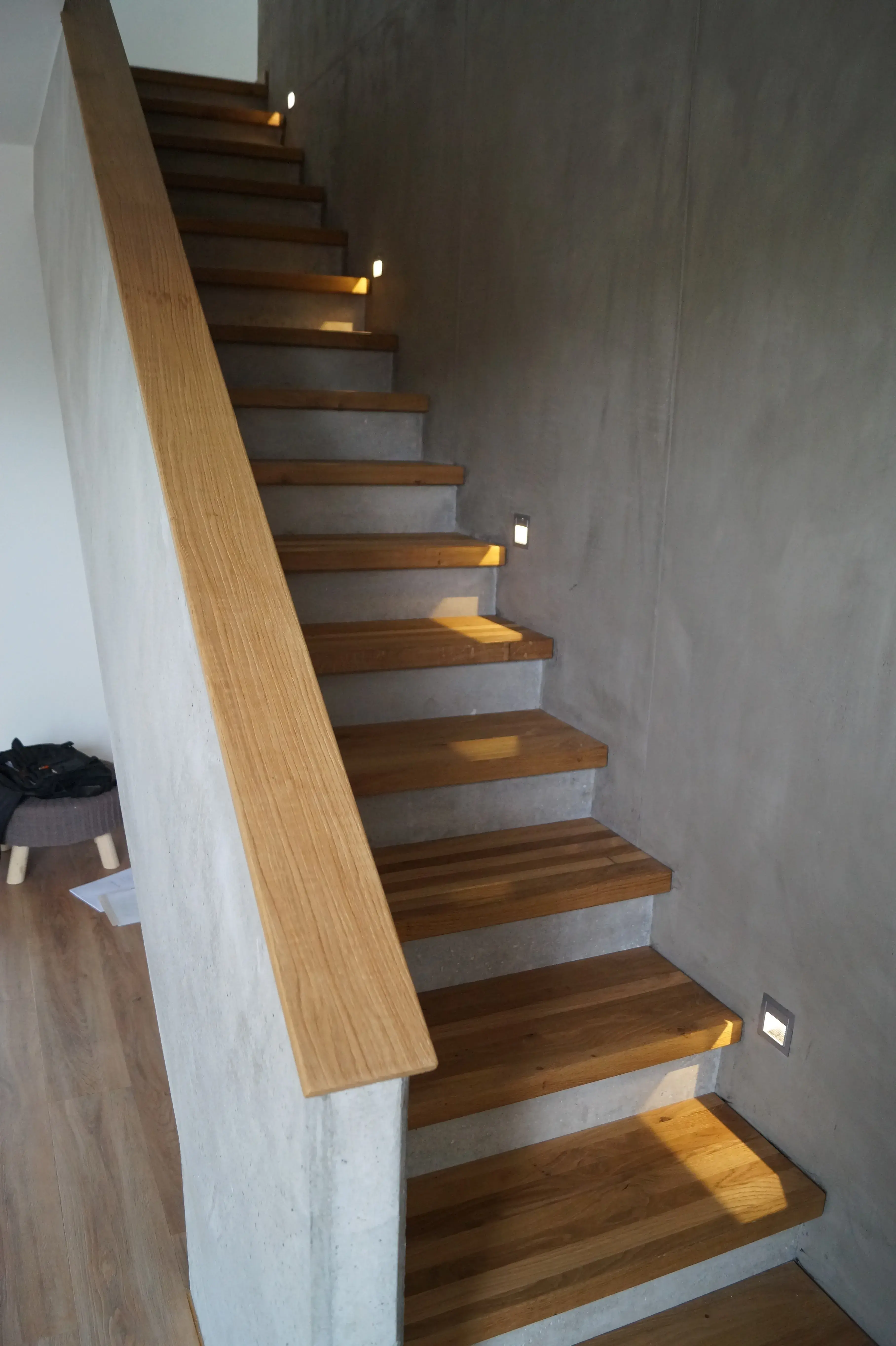 Moderne Holztreppe mit Eichenstufen, Holzhandlauf und integrierter Beleuchtung an Wänden in Betonoptik