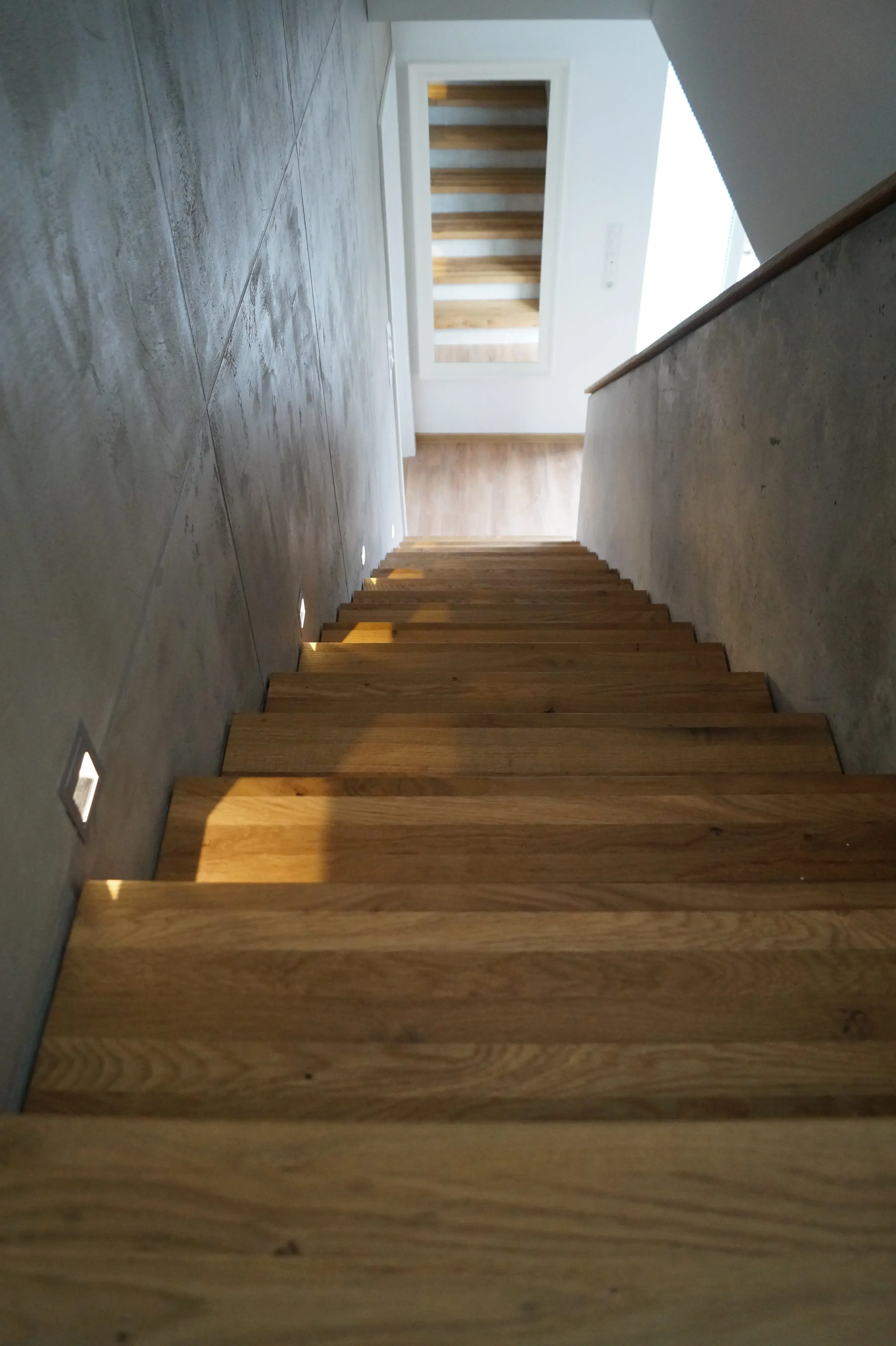 Moderne Holztreppe mit integrierter Stufenbeleuchtung und Wänden in Betonoptik