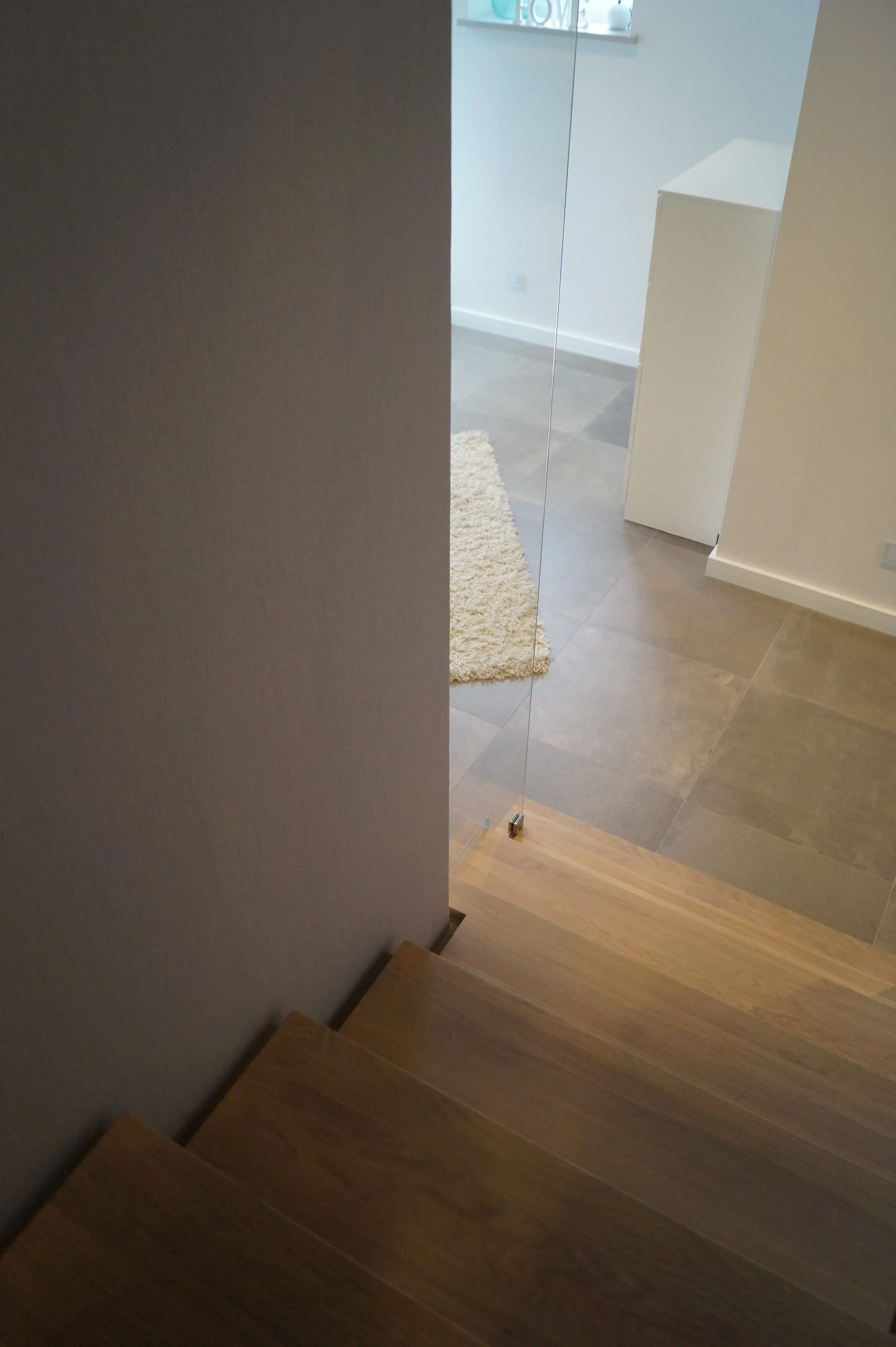 Moderne Holztreppe mit Glasgeländer und grauen Bodenfliesen in hellem Wohnraum