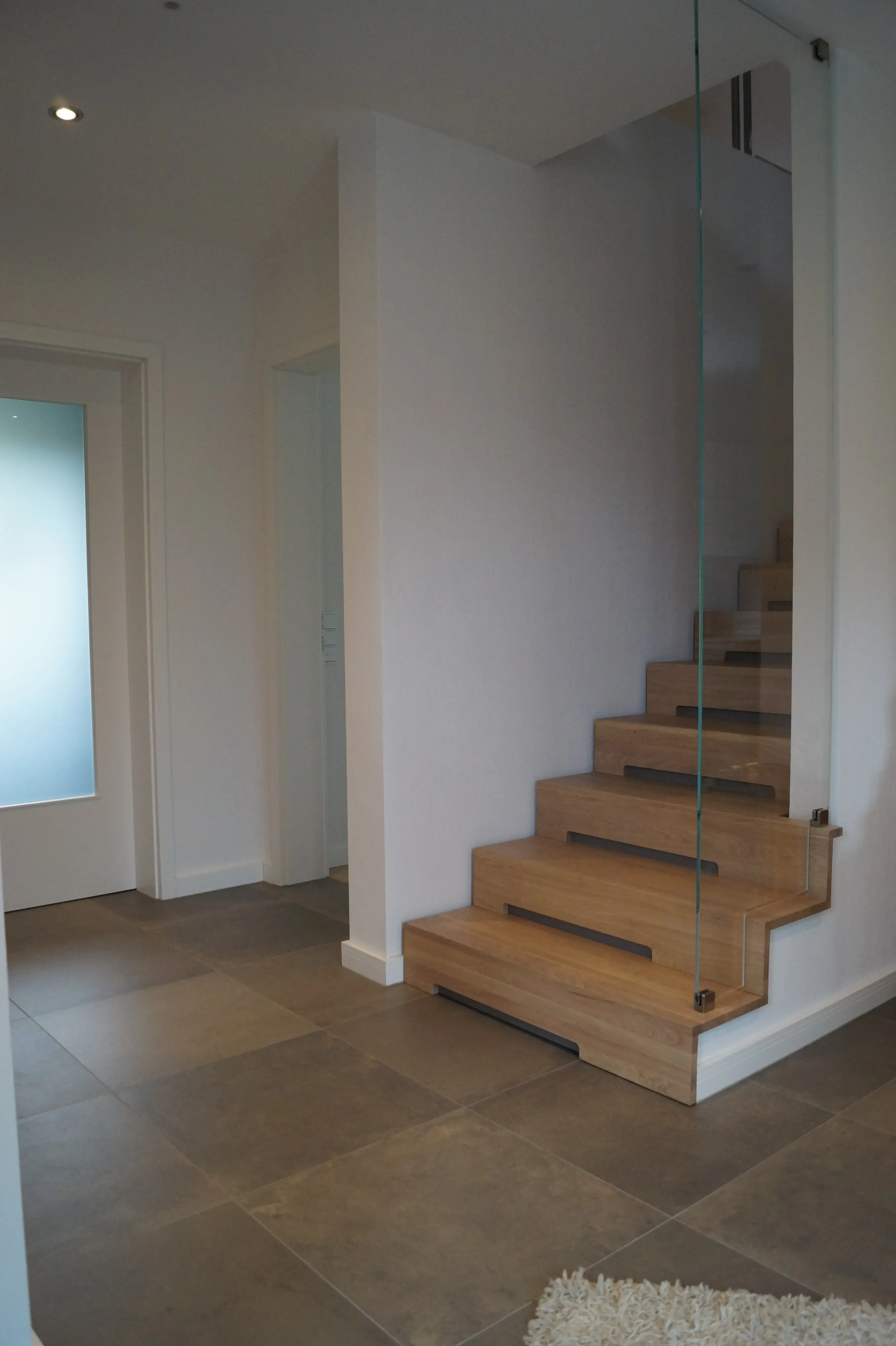 Moderne Holztreppe mit Glasgeländer und integrierter Beleuchtung im hellen Wohnbereich