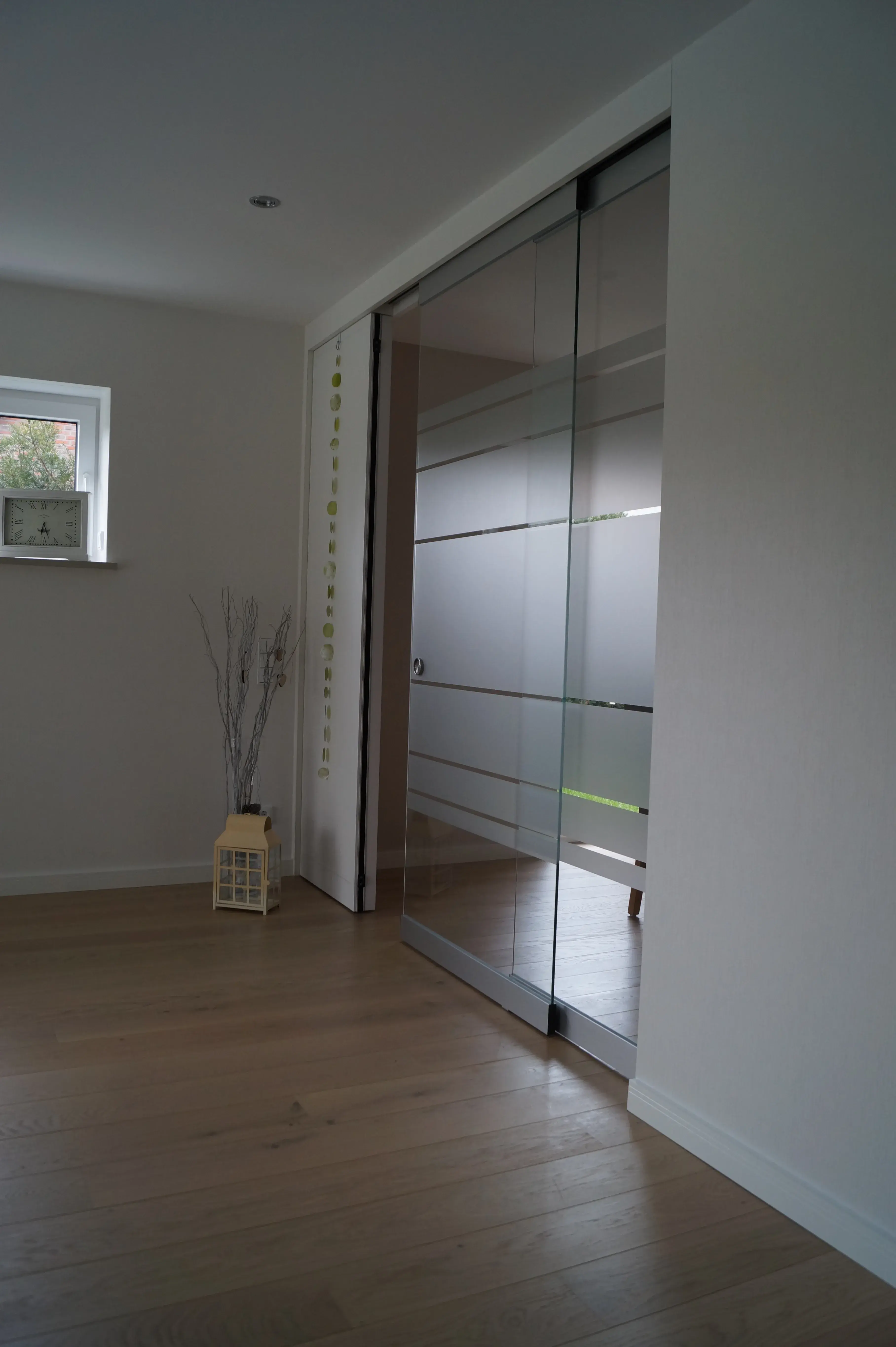 Große Glasschiebetür mit satinierten Streifen als moderner Raumteiler im hellen Wohnbereich