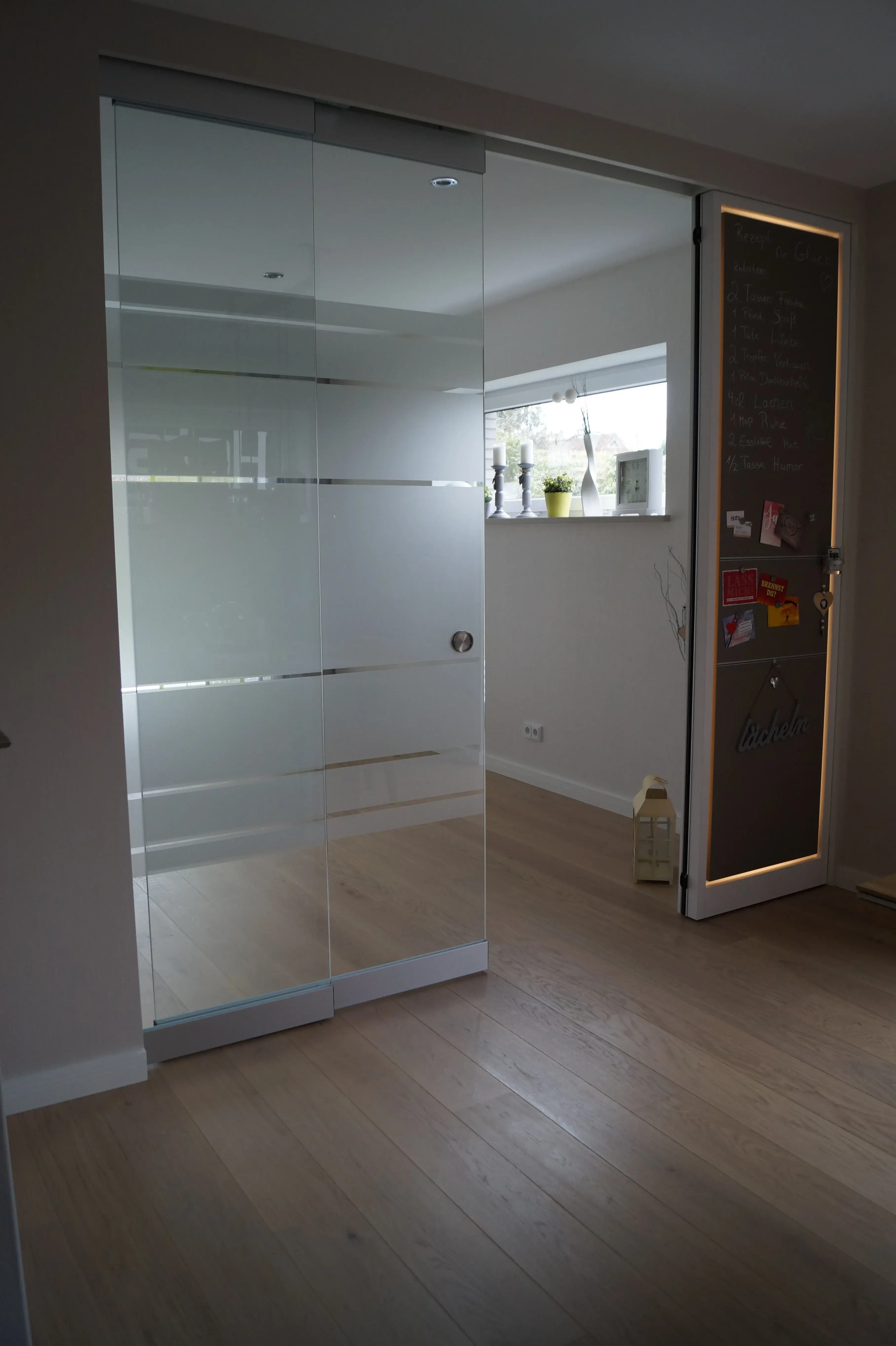 Glasschiebetür mit satinierten Streifen und beleuchteter Tafel als moderner Raumteiler