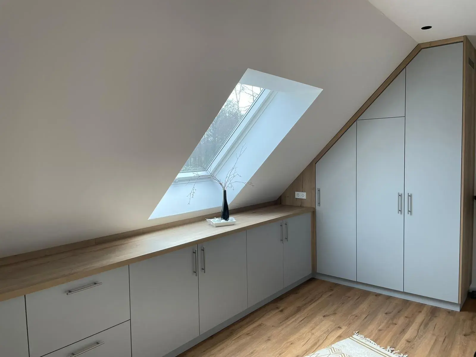 Maßgefertigter Einbauschrank unter der Dachschräge mit weißen Fronten und Holzdetails