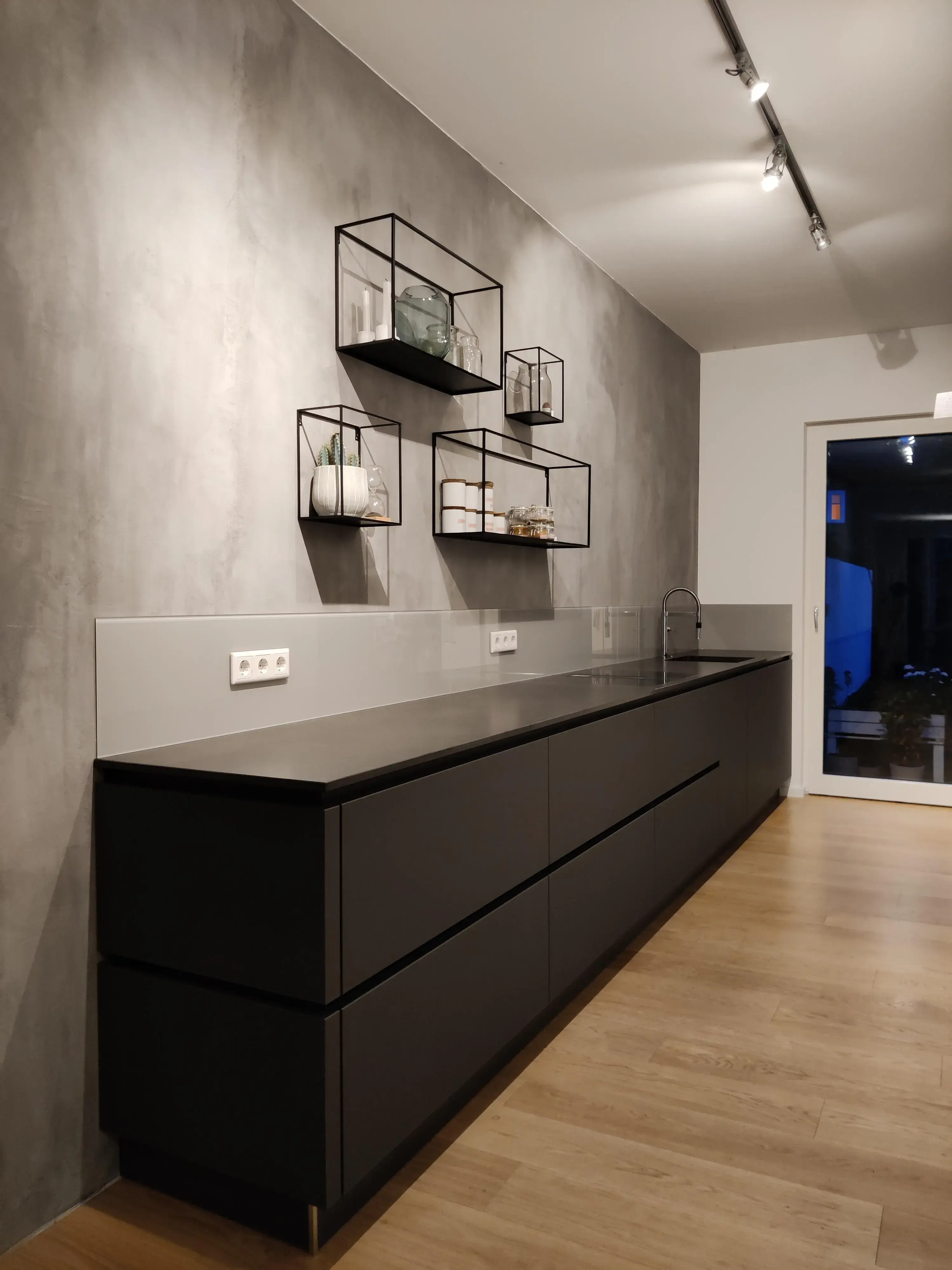 Grifflose anthrazitfarbene Küchenzeile mit dunkler Arbeitsplatte, Betonoptik und offenen Metallregalen