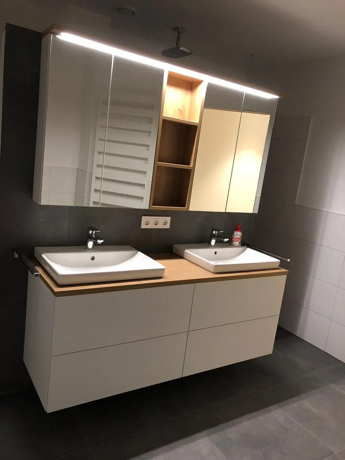 Modernes Badezimmer mit weißem Doppelwaschtisch, grifflosen Badmöbeln, Holzarbeitsplatte und beleuchtetem Spiegelschrank