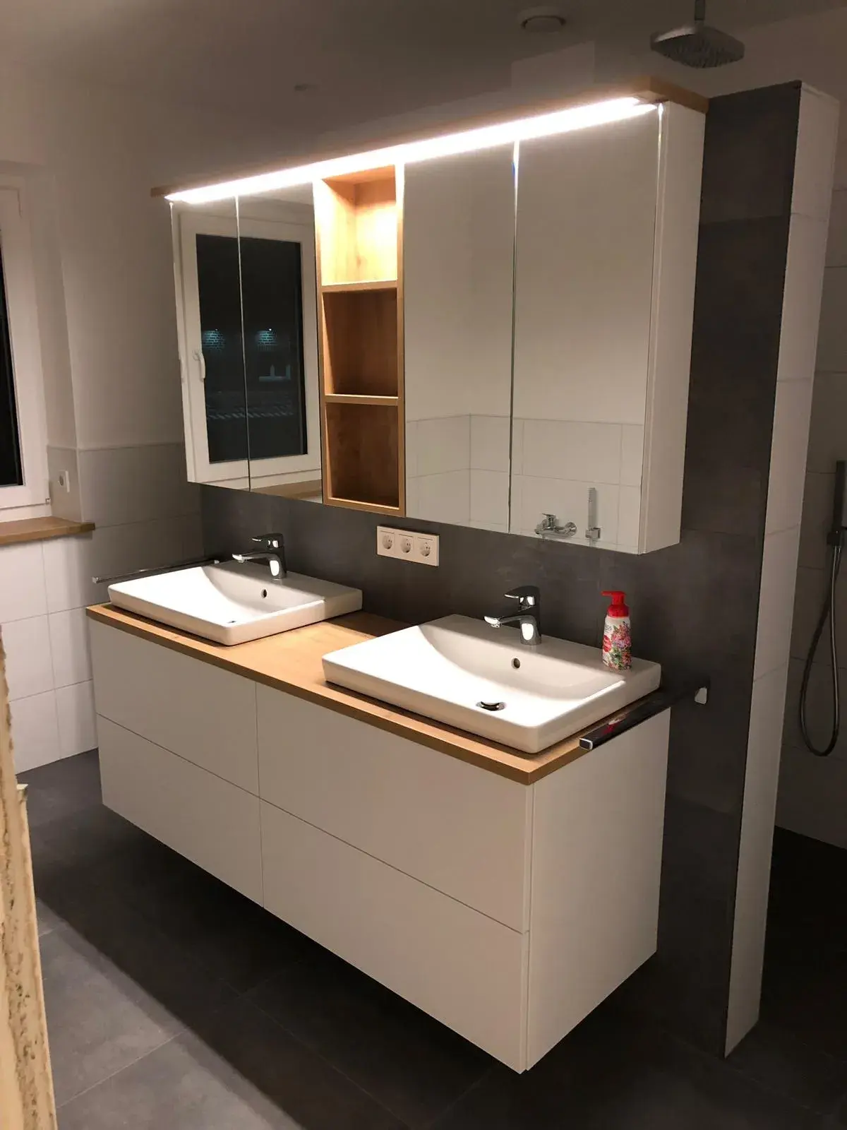 Modernes Badezimmer mit weißen grifflosen Badmöbeln, Doppelwaschtisch, Holzarbeitsplatte und beleuchtetem Spiegelschrank