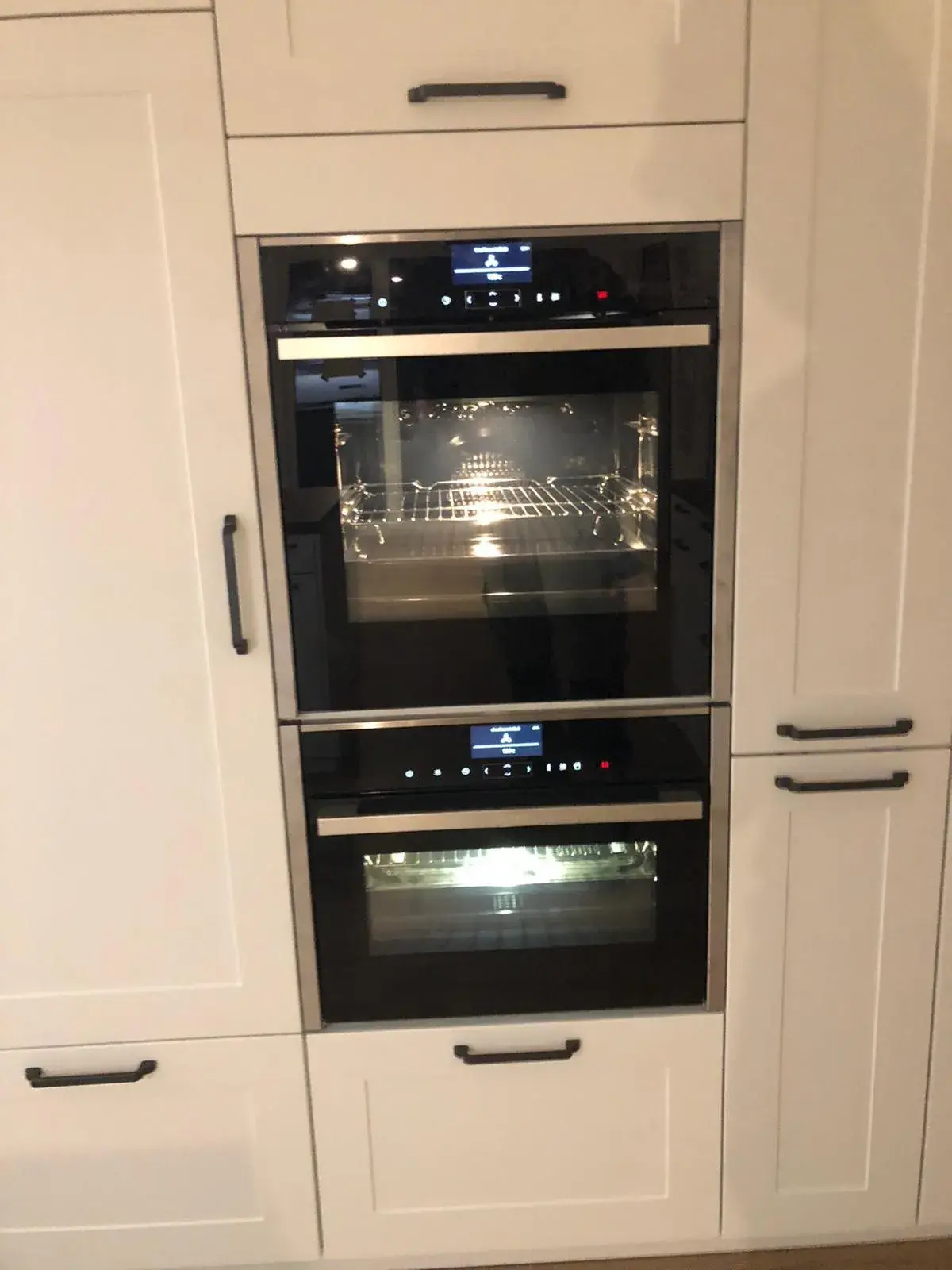 Integrierter Backofen und Dampfgarer in weißer Landhausküche mit klassischen Rahmenfronten und schwarzen Griffen
