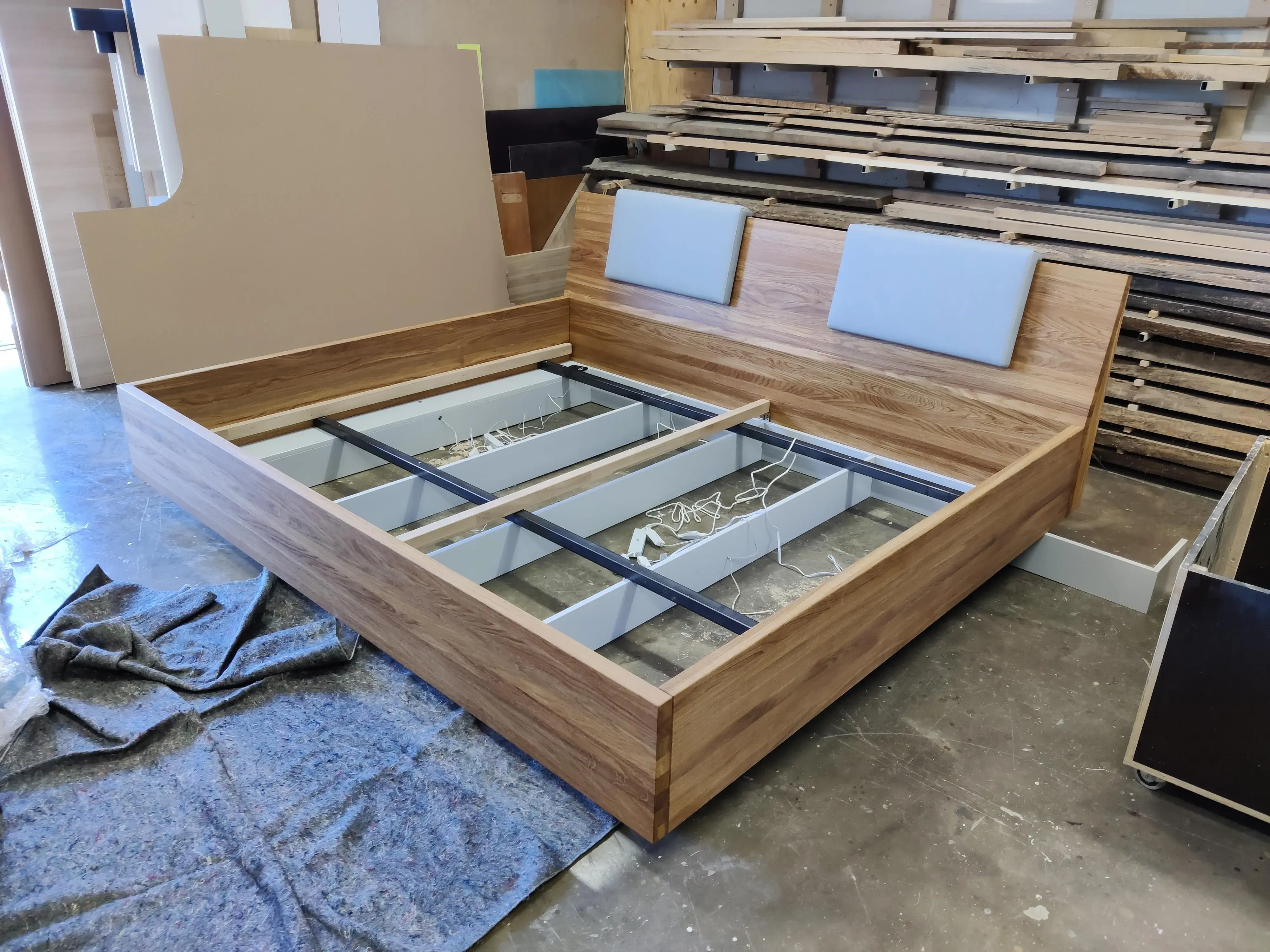Maßgefertigtes Doppelbett aus Holz mit gepolstertem Kopfteil während der Fertigung in der Tischlerei