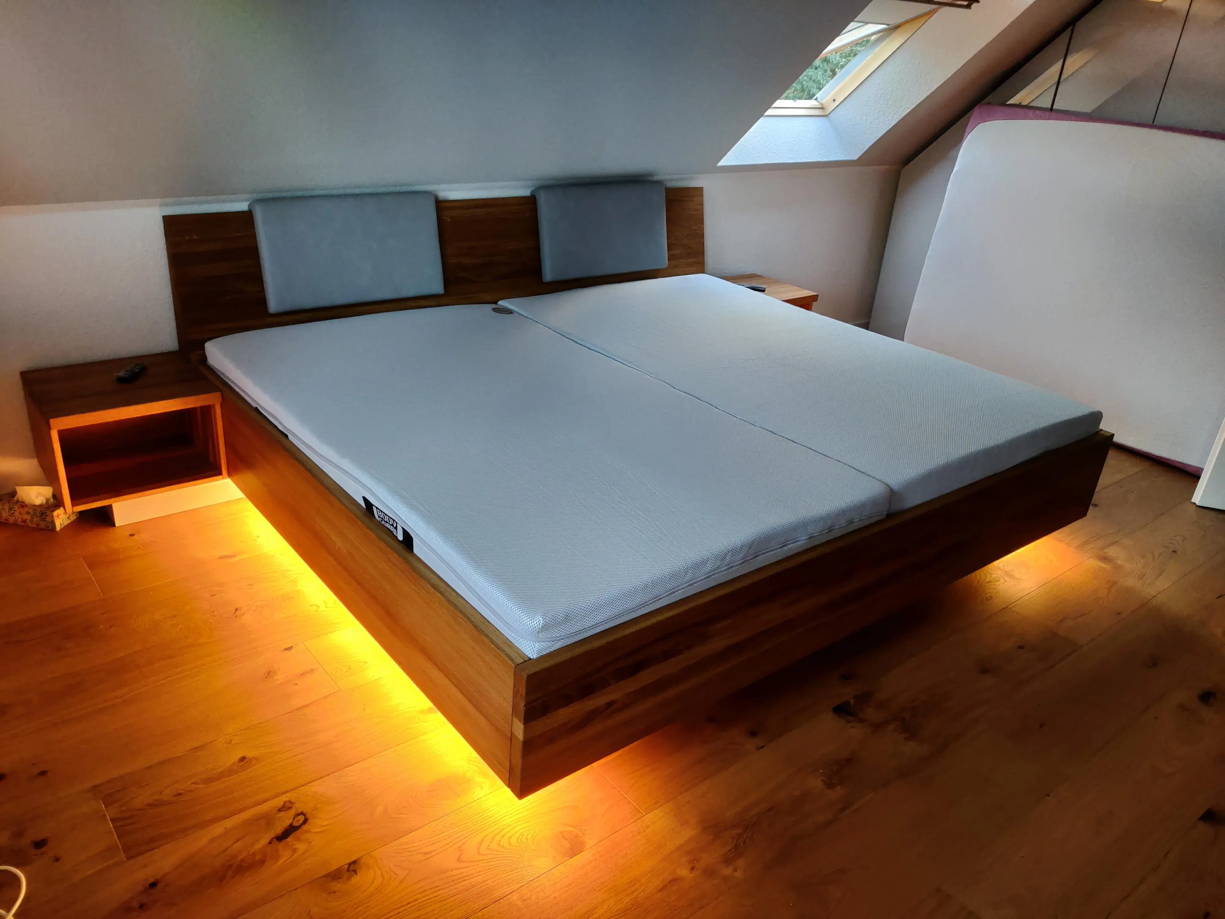 Maßgefertigtes Doppelbett aus Holz mit gepolstertem Kopfteil, Nachttischen und indirekter Beleuchtung unter der Dachschräge