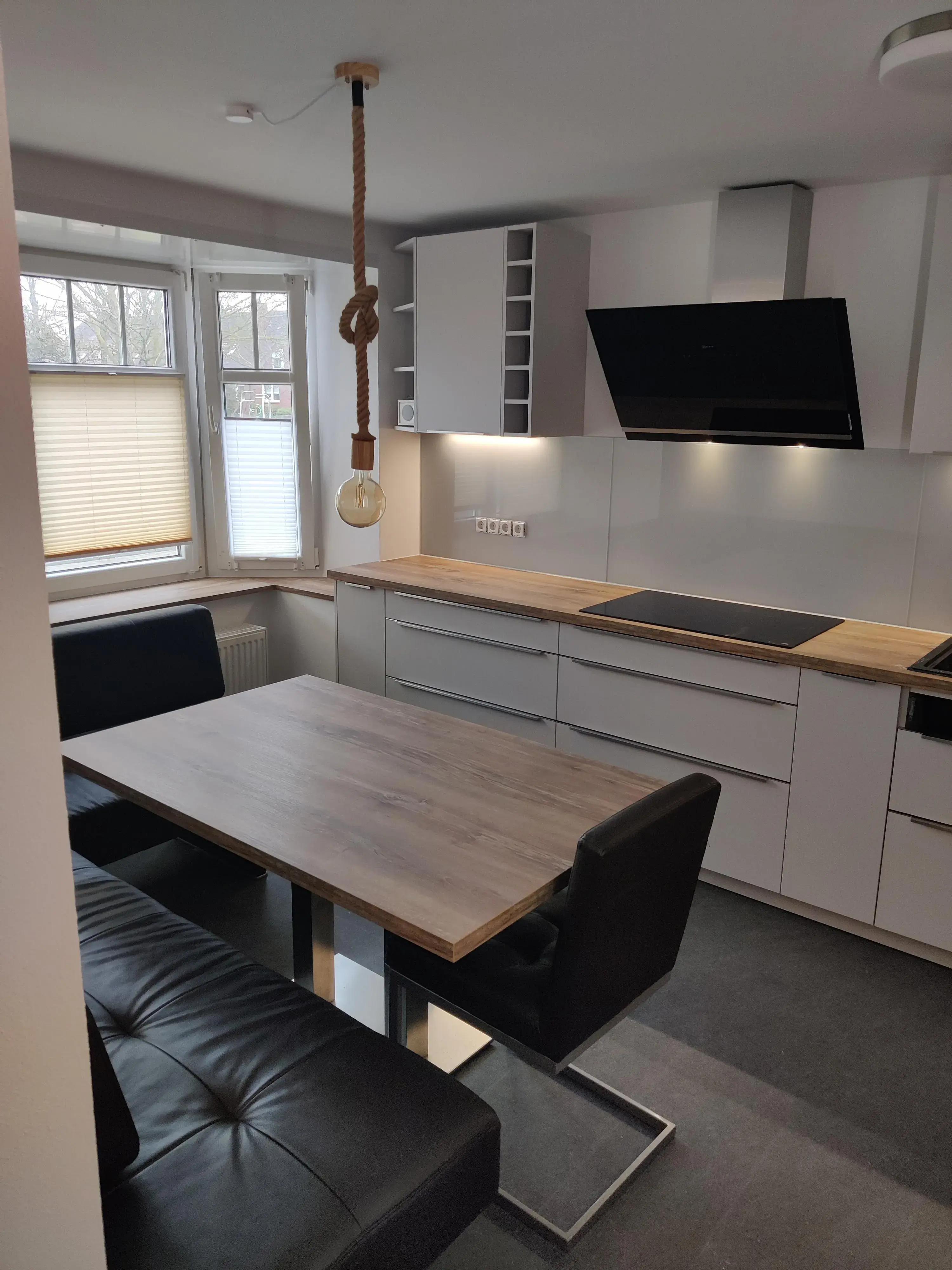Moderne graue Küche mit Holzarbeitsplatte, Essplatz und schwarzer Sitzbank