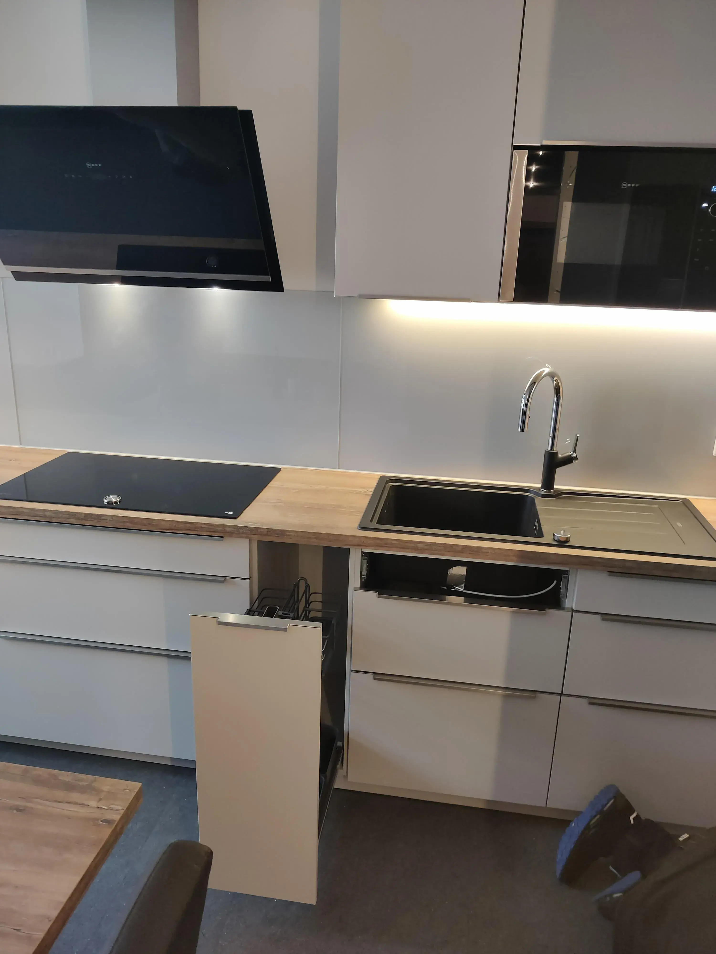 Moderne graue Küche mit Holzarbeitsplatte, schwarzen Einbaugeräten und beleuchteter Vitrine