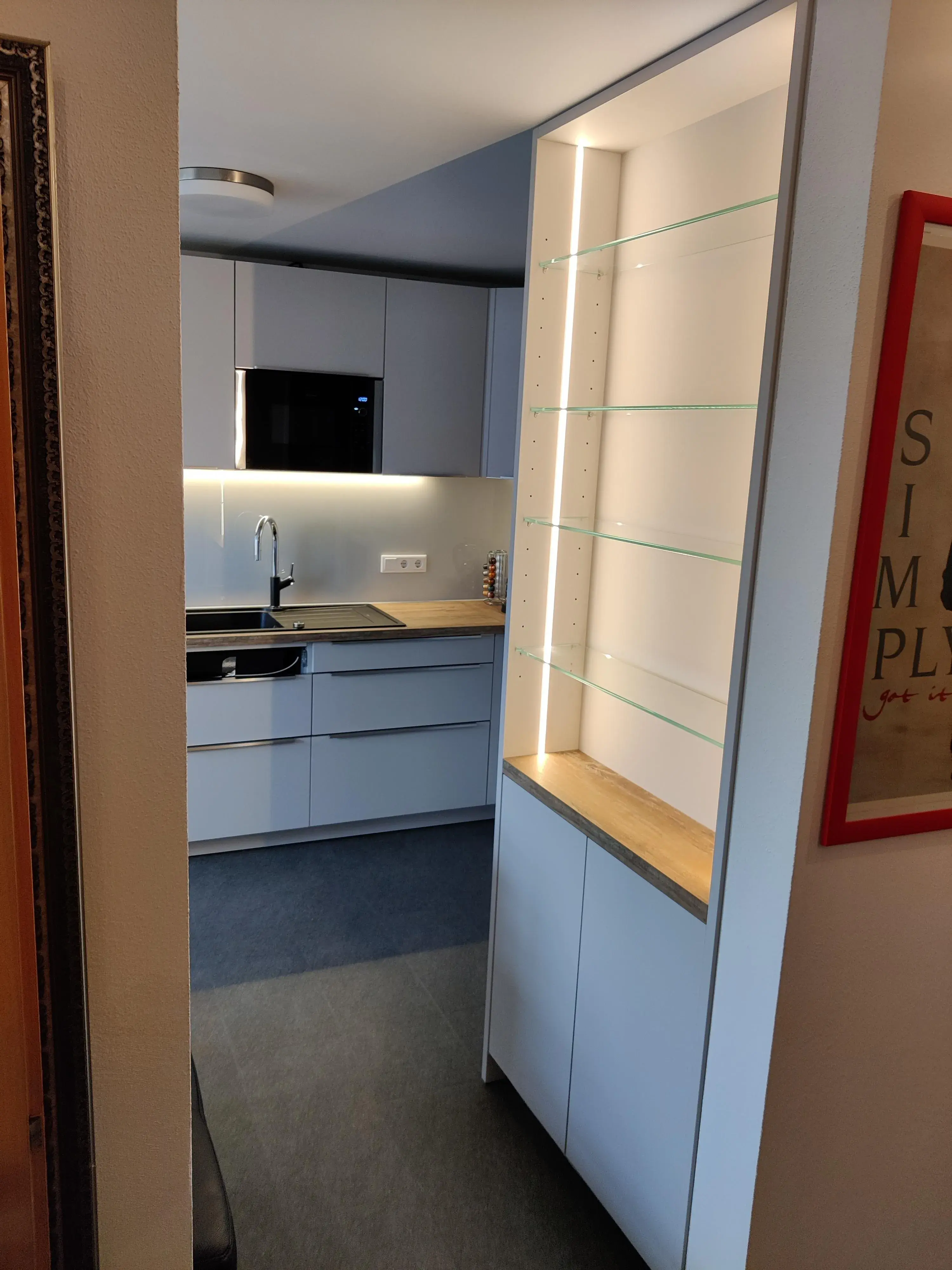 Moderne graue Küche mit Holzarbeitsplatte und beleuchteter Vitrine mit Glasböden