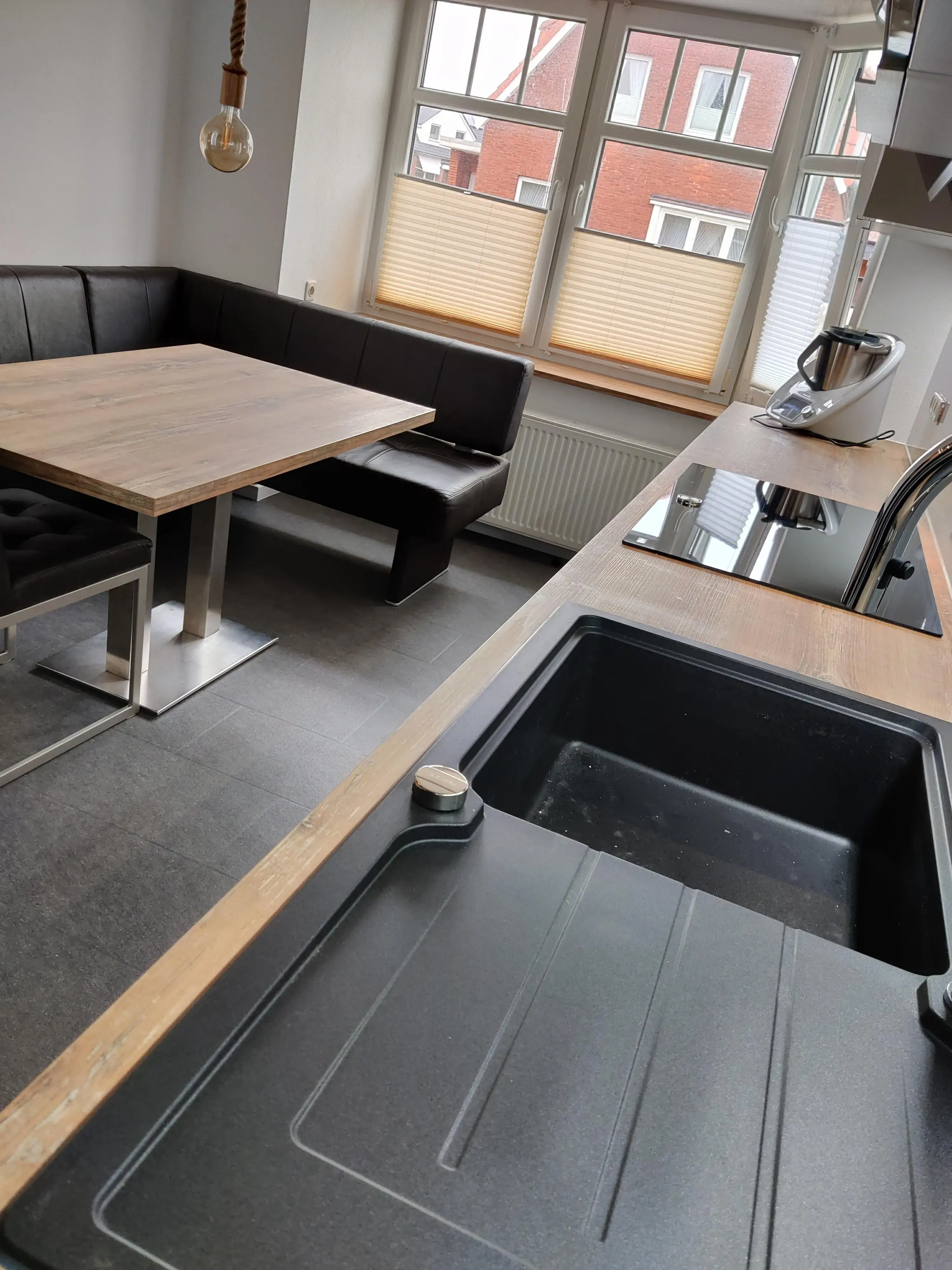 Moderne Küche mit Holzarbeitsplatte, schwarzer Spüle und Essbereich mit Eckbank am Fenster