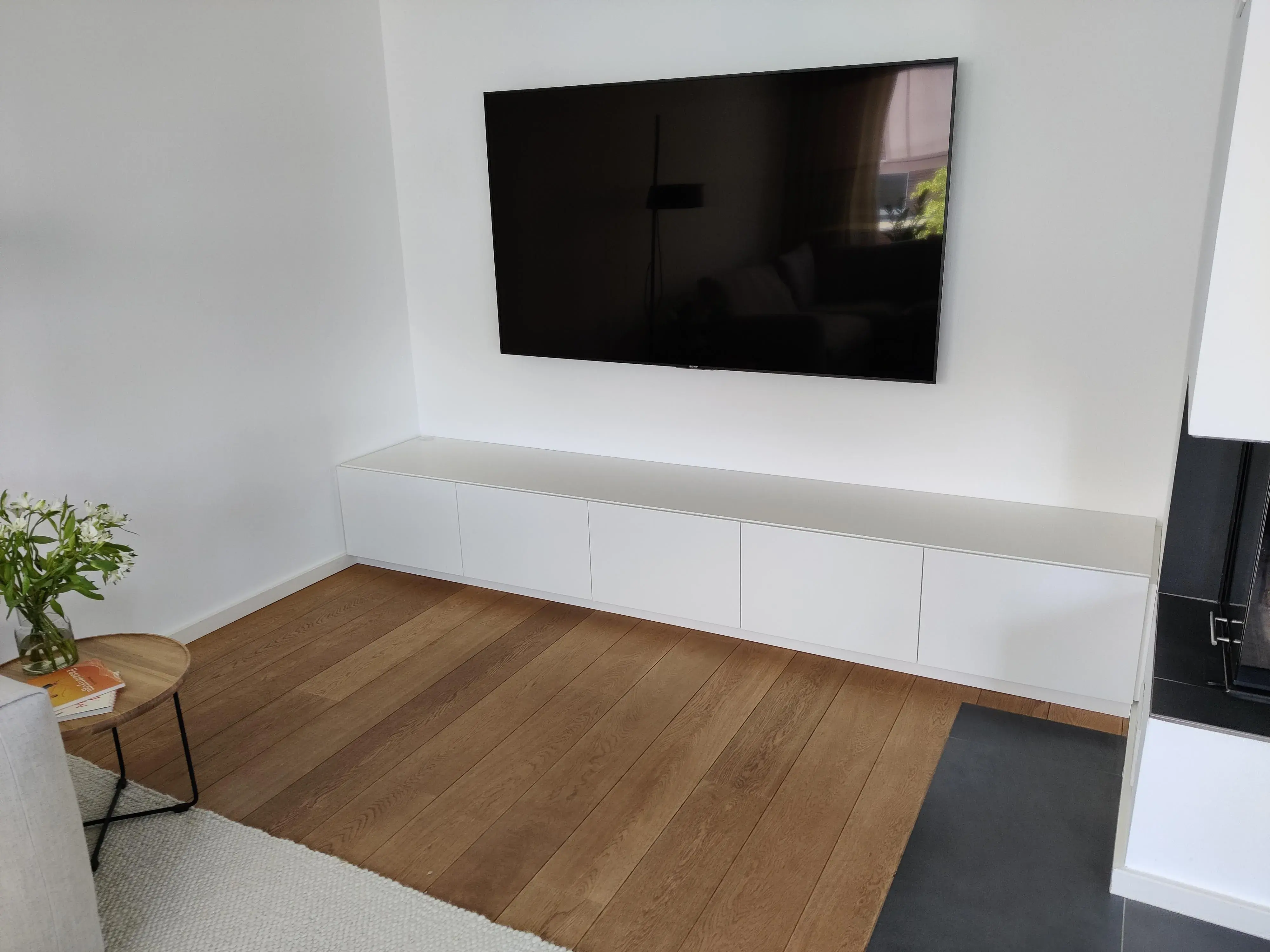 Maßgefertigtes weißes TV-Lowboard mit grifflosen Fronten unter einem wandmontierten Fernseher