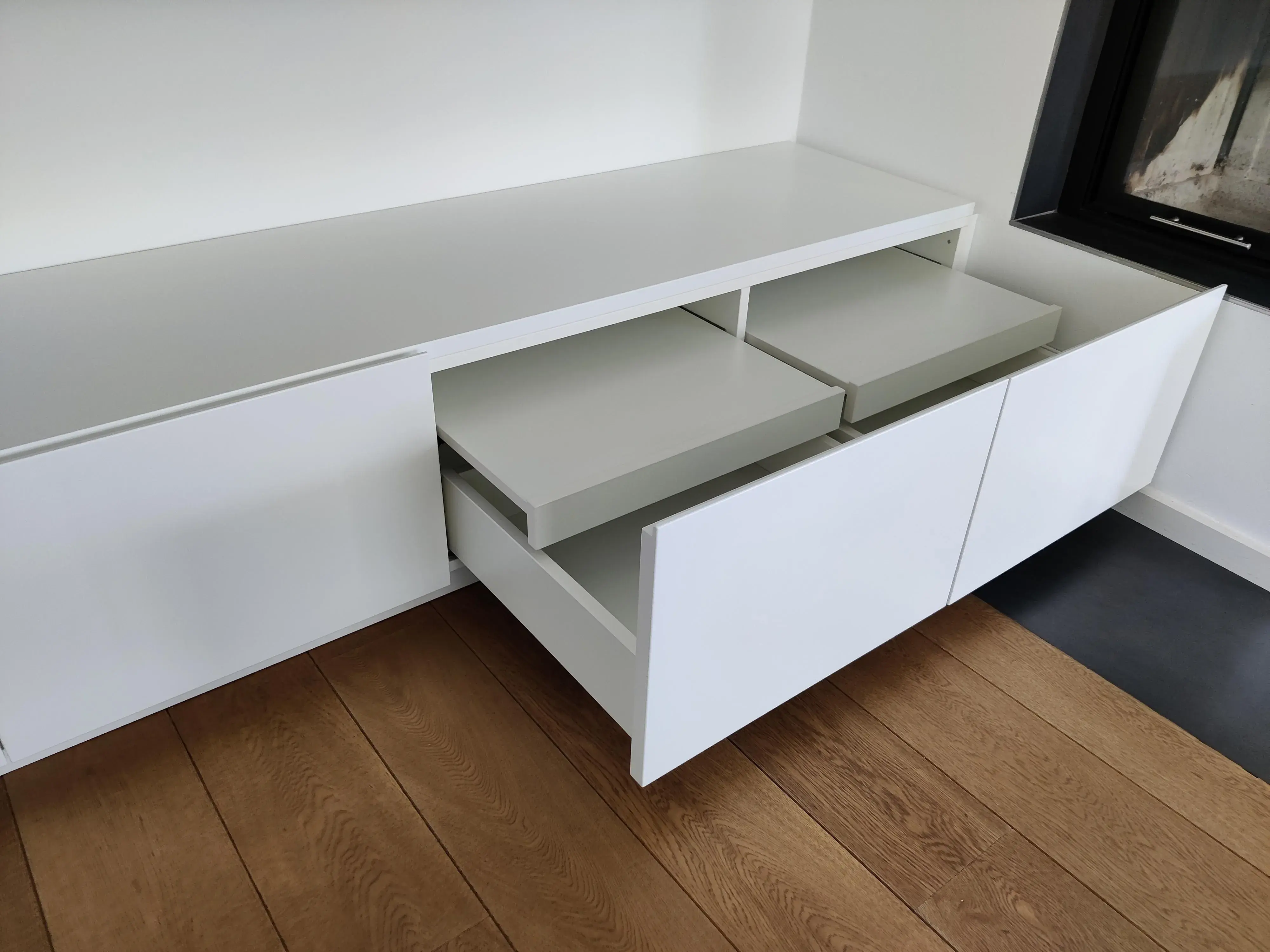 Maßgefertigtes weißes Sideboard mit grifflosen Fronten, geöffneten Schubladen und praktischen Innenauszügen