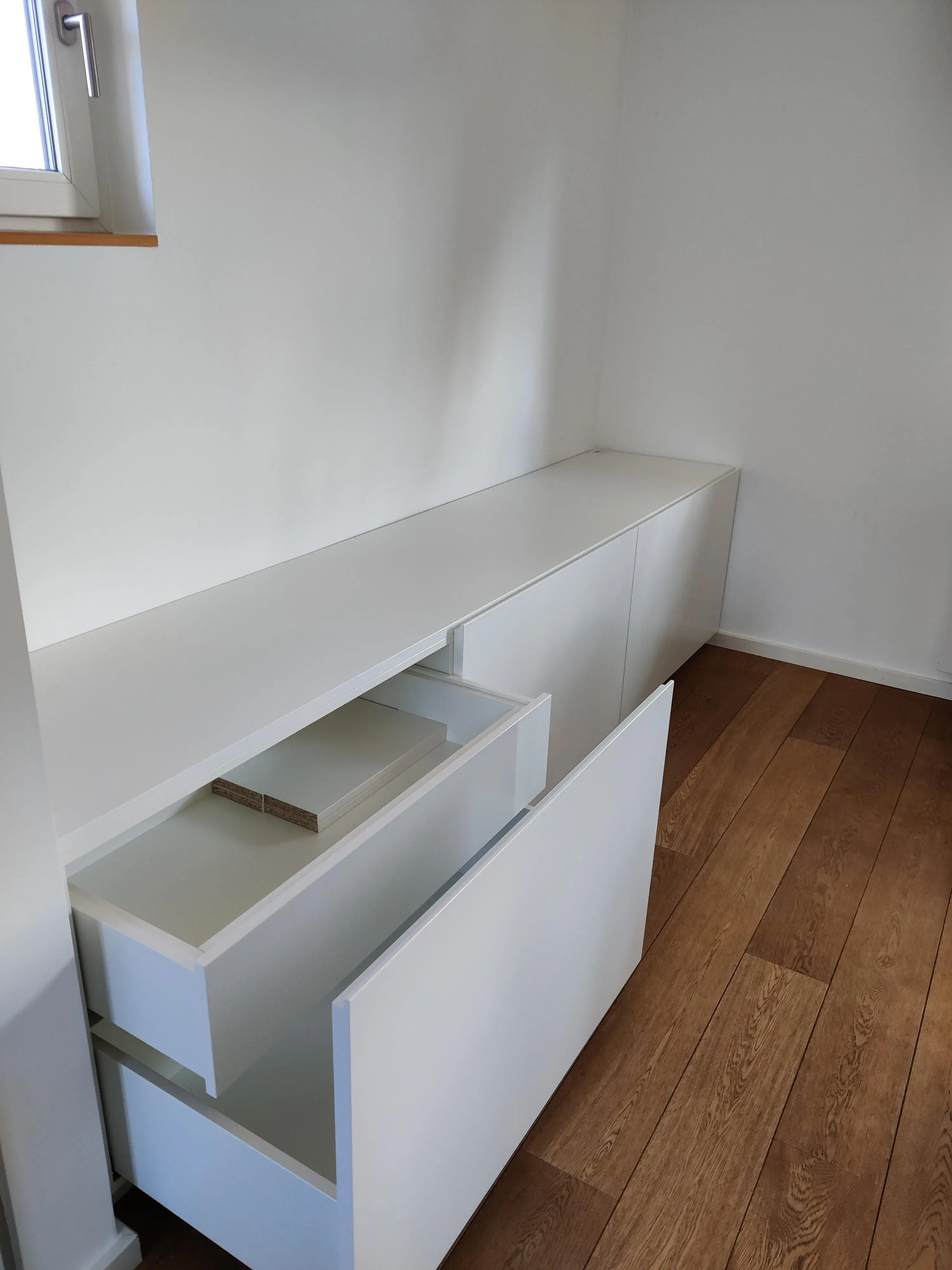 Maßgefertigtes weißes Sideboard mit grifflosen Fronten und geöffneten Schubladen