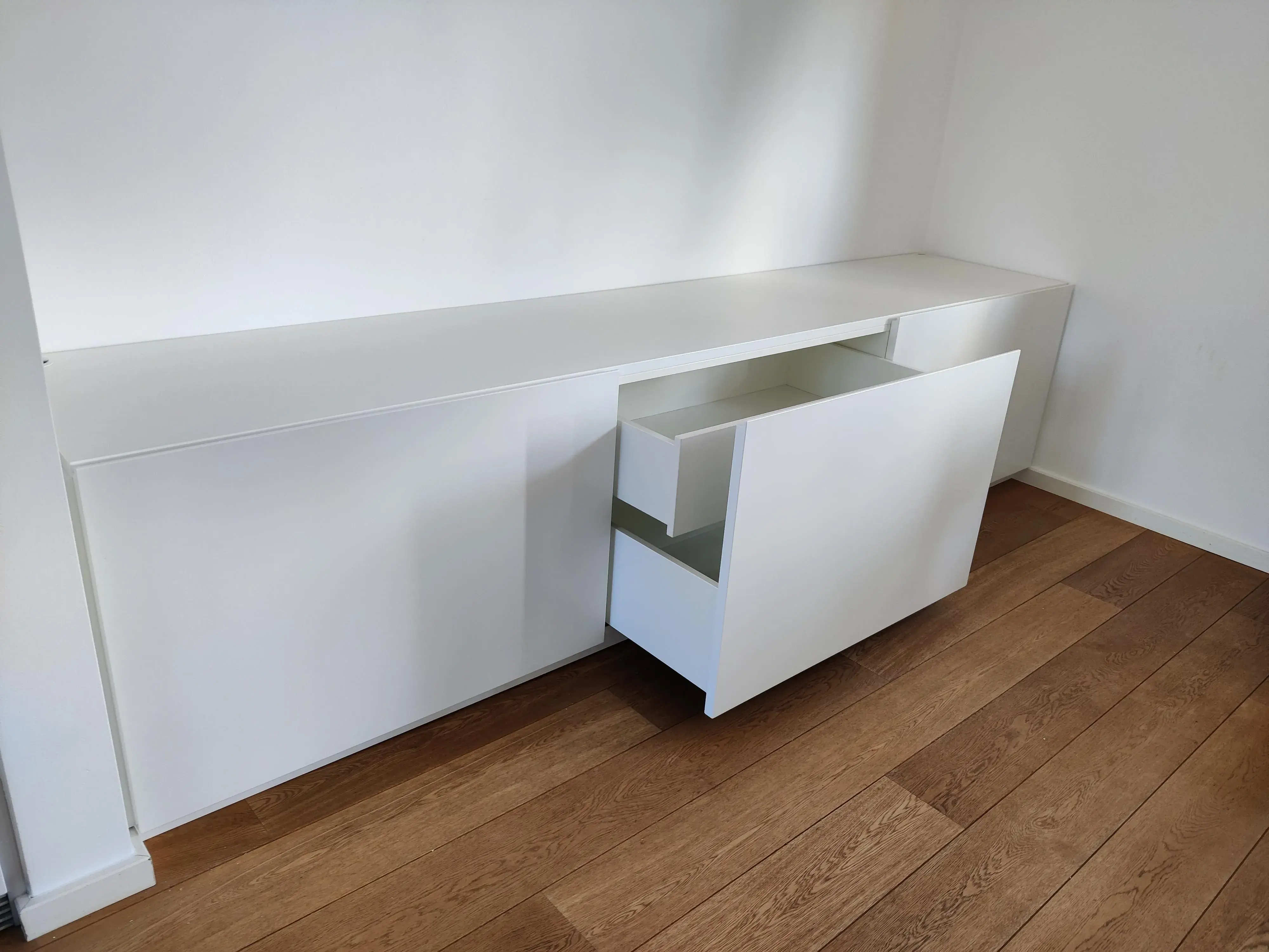 Maßgefertigtes weißes Sideboard mit grifflosen Fronten und geöffneten Schubladen auf Holzboden