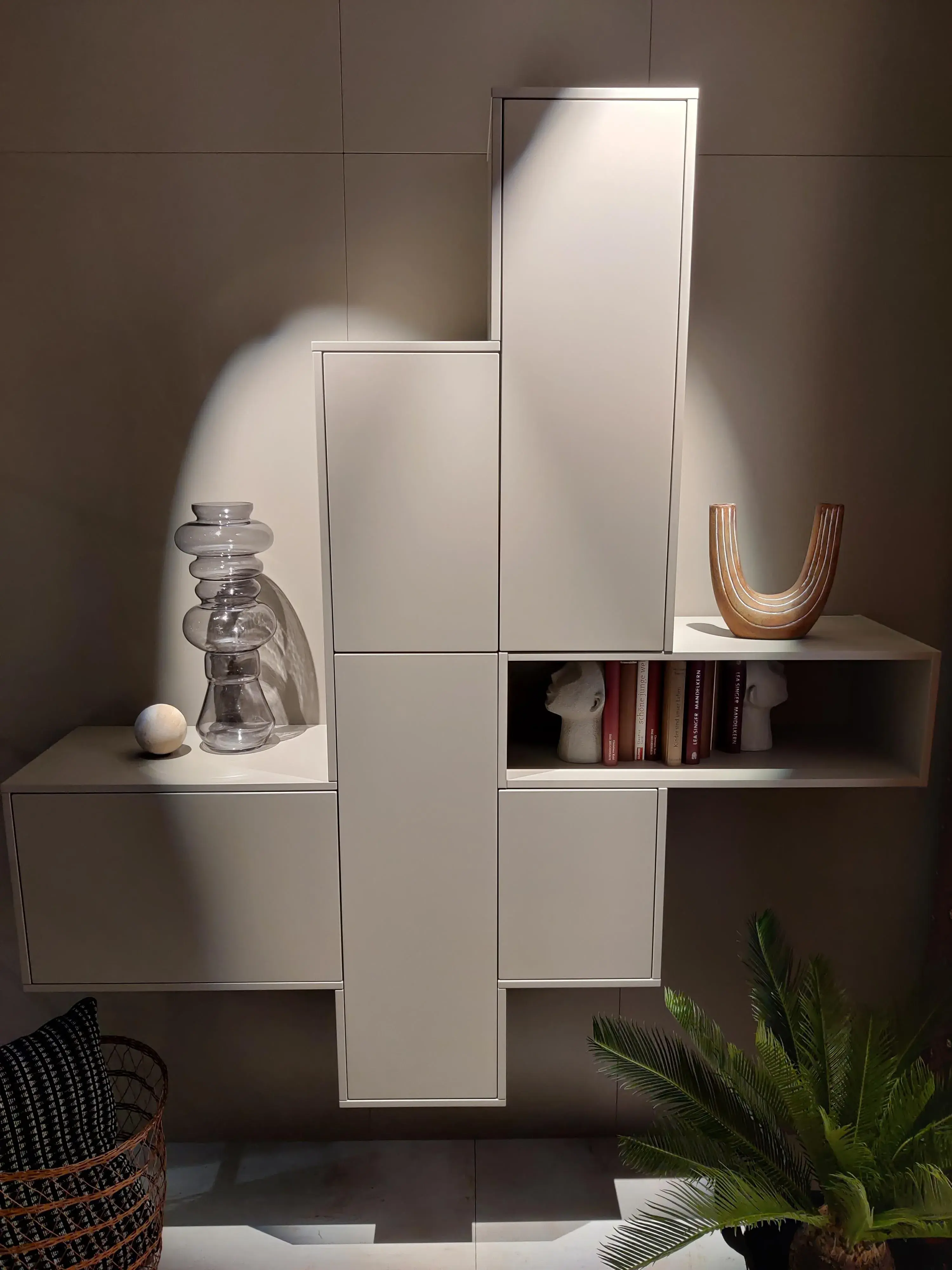 Moderne weiße Wohnwand mit asymmetrischen Schränken, offenem Regal und dekorativen Wohnaccessoires