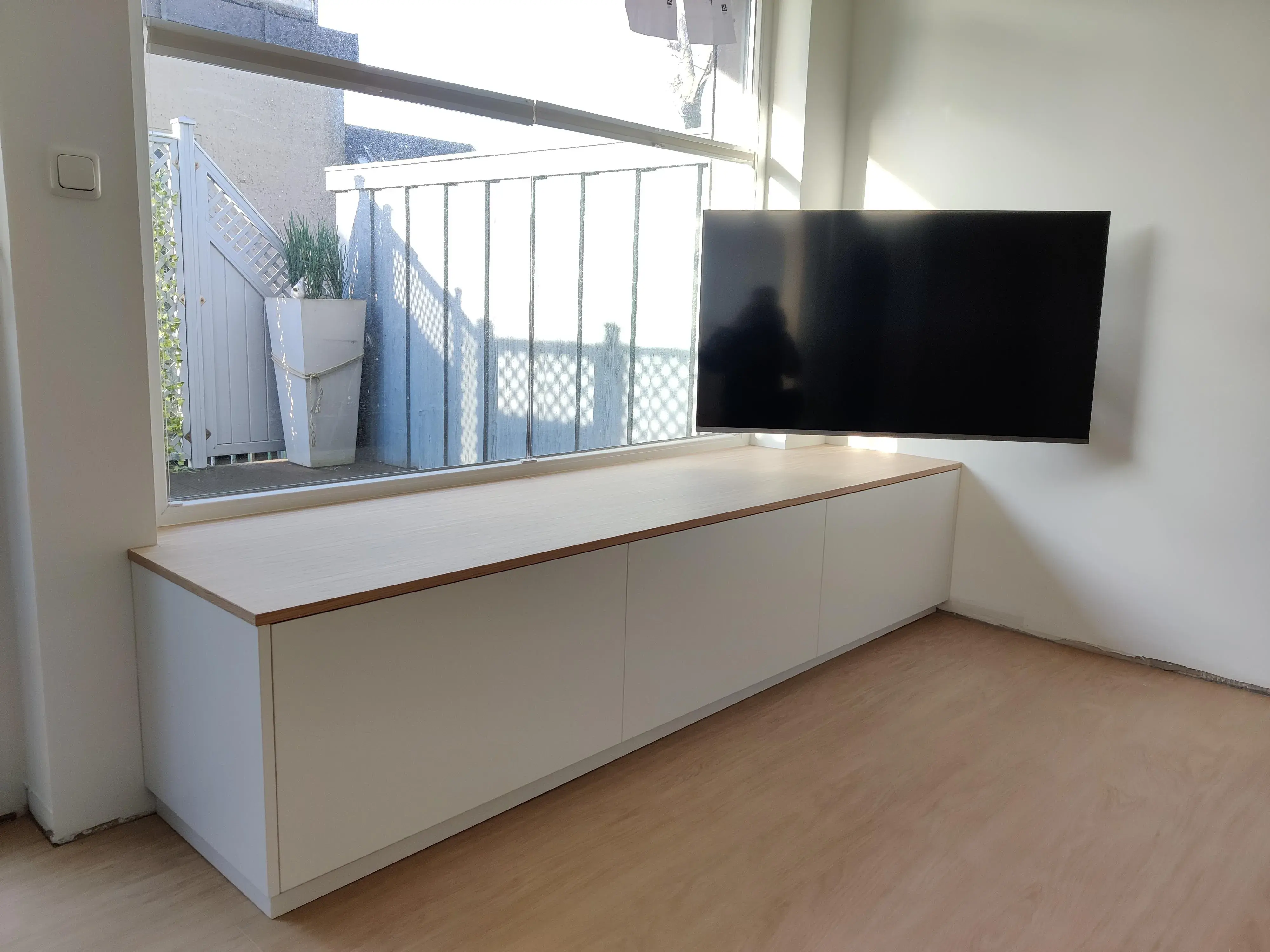 Maßgefertigtes weißes Lowboard mit Holzplatte und wandmontiertem Fernseher vor großer Fensterfront