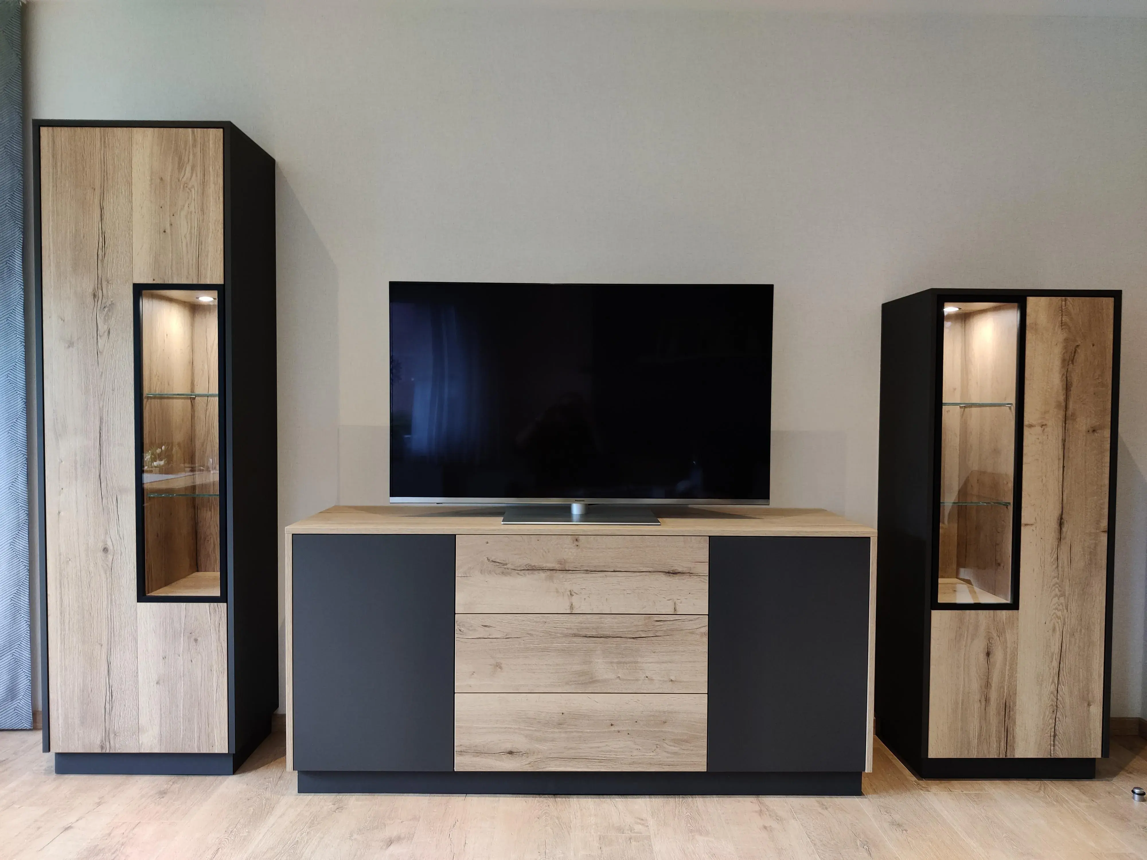Maßgefertigte Wohnwand mit TV-Möbel und beleuchteten Glasvitrinen in Holz und Anthrazit
