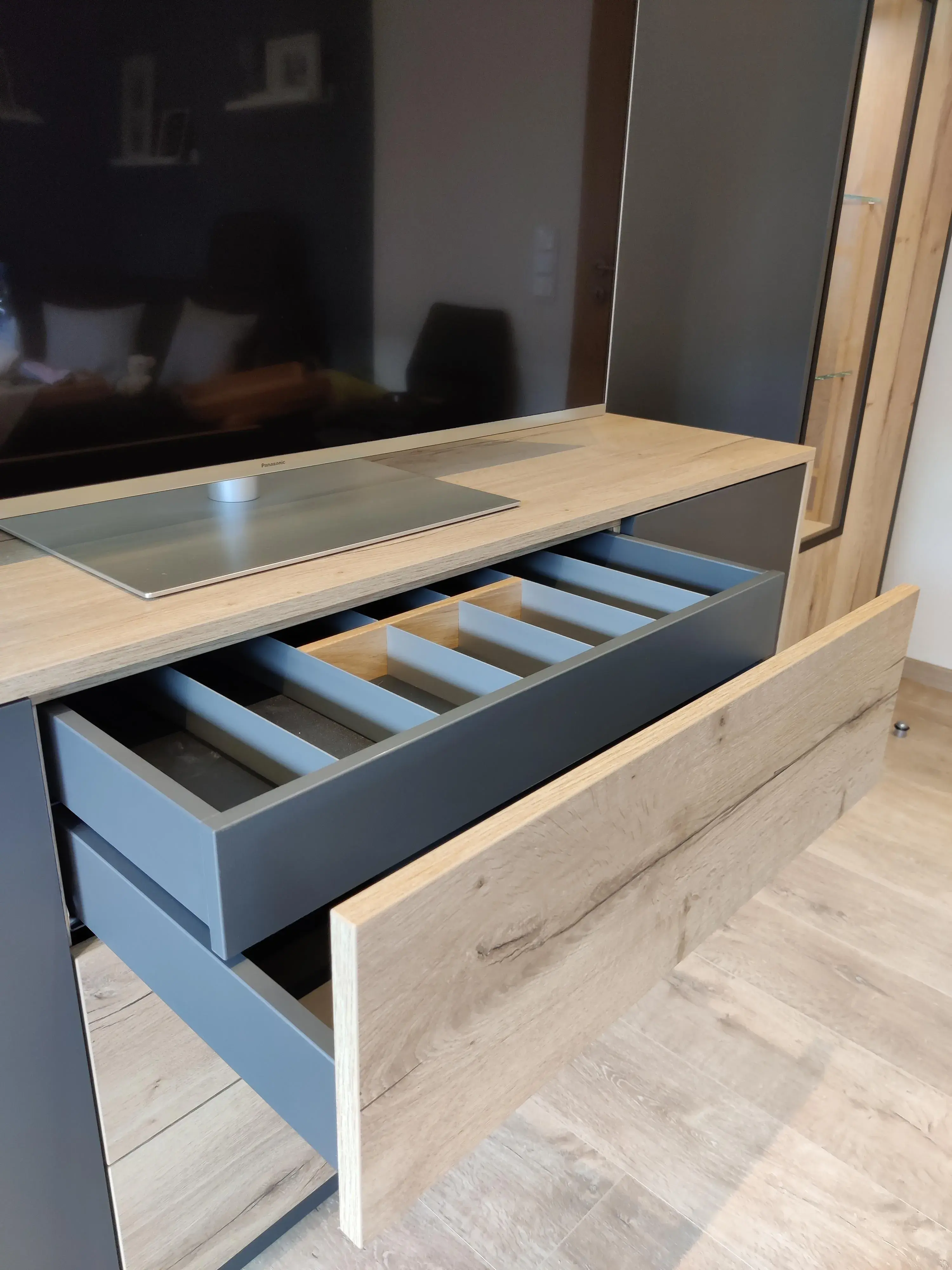 Detail eines maßgefertigten TV-Möbels in Holz und Anthrazit mit geöffneten Schubladen und praktischer Inneneinteilung