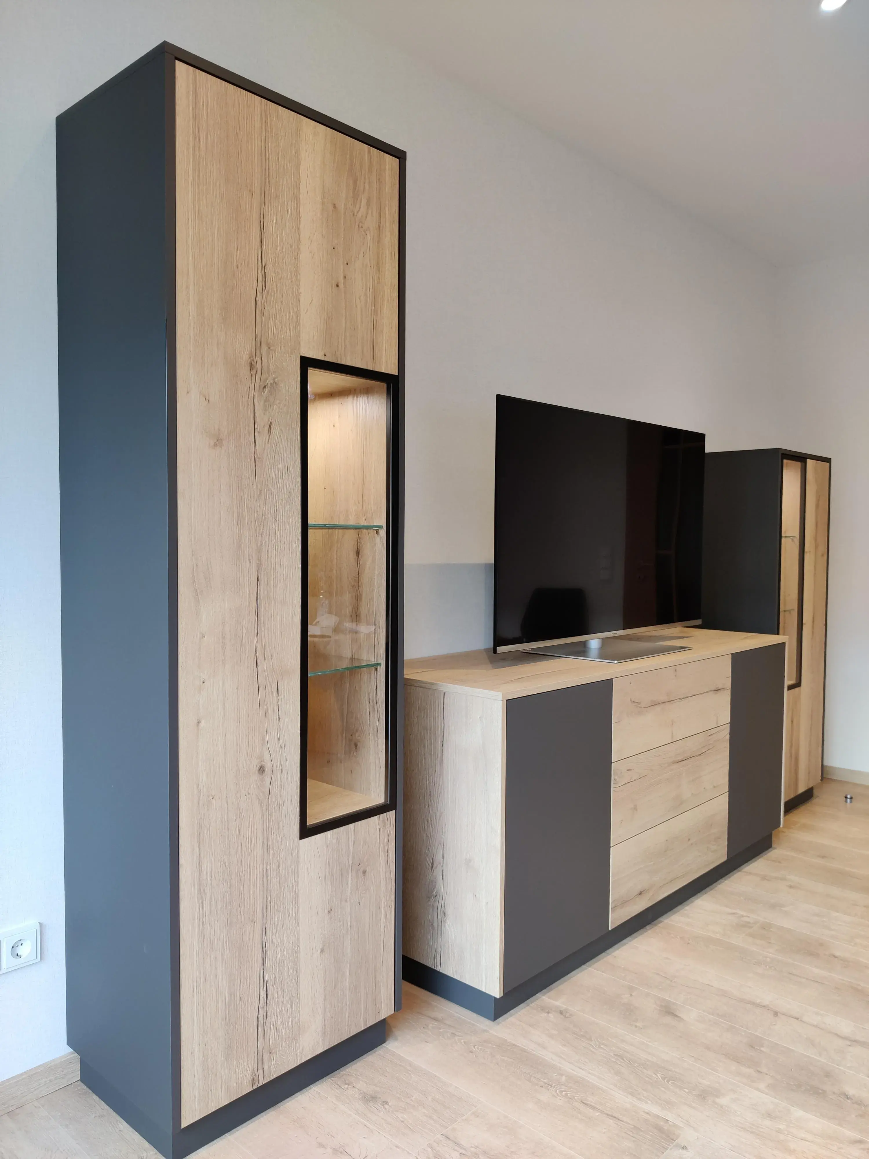 Individuelle Wohnwand mit TV-Möbel und beleuchteten Vitrinen in Holz und Anthrazit