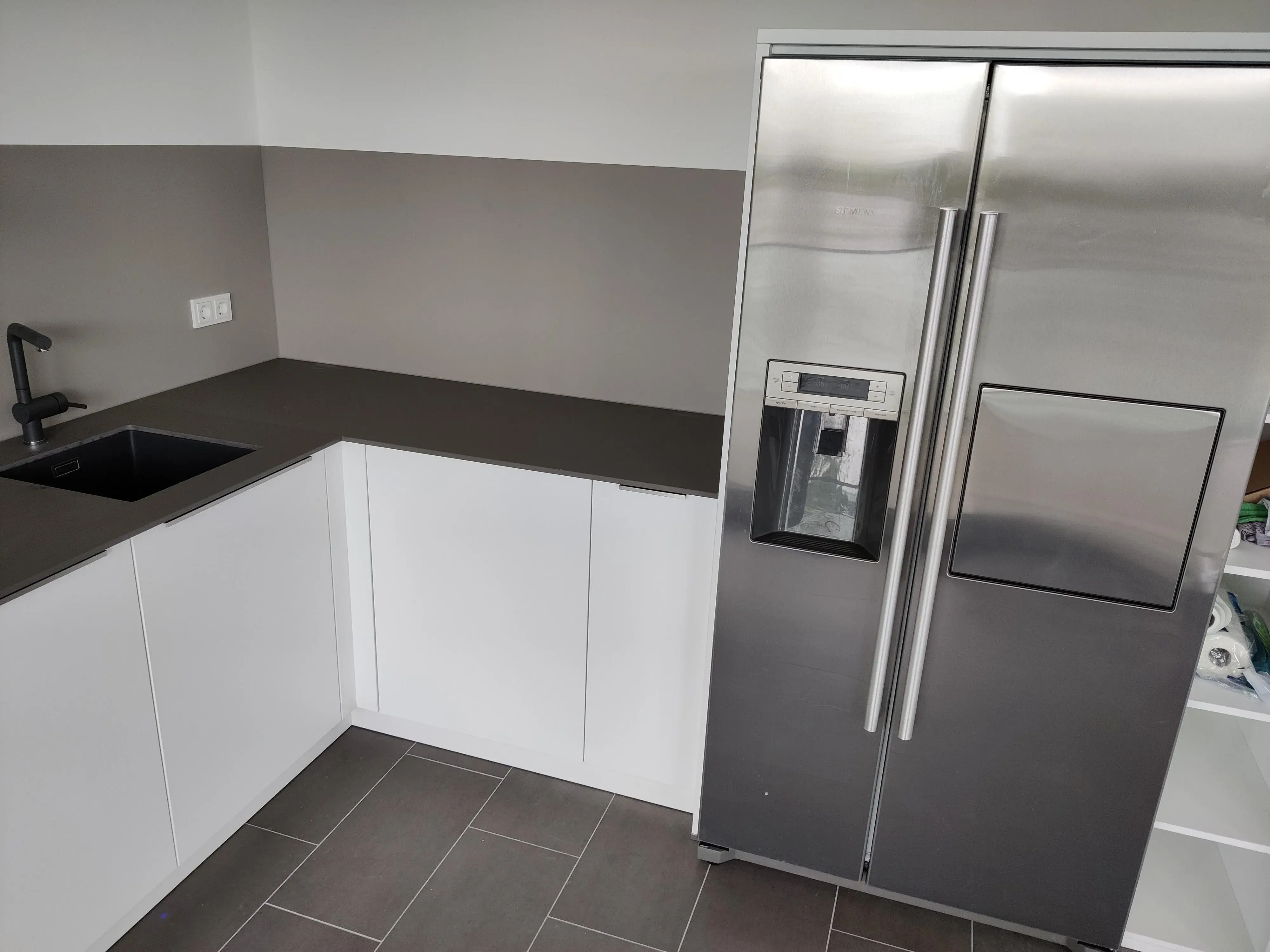 Moderne weiße Küche mit dunkler Arbeitsplatte, schwarzer Spüle und Side-by-Side-Kühlschrank