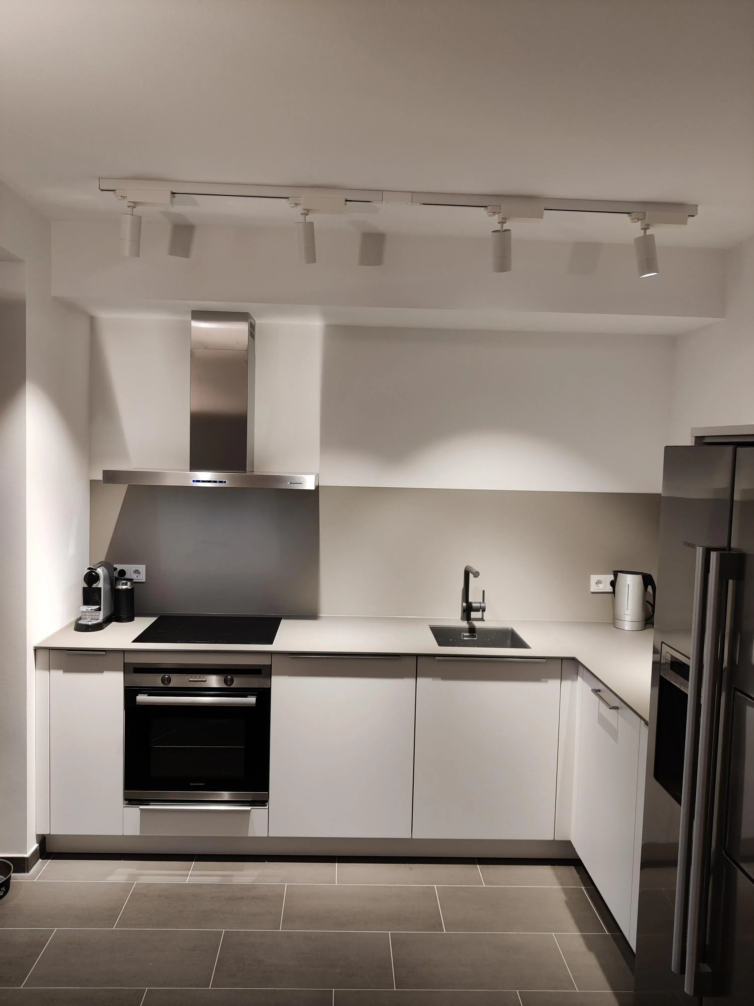 Moderne weiße Winkelküche mit heller Arbeitsplatte, Einbaubackofen und Edelstahl-Dunstabzugshaube