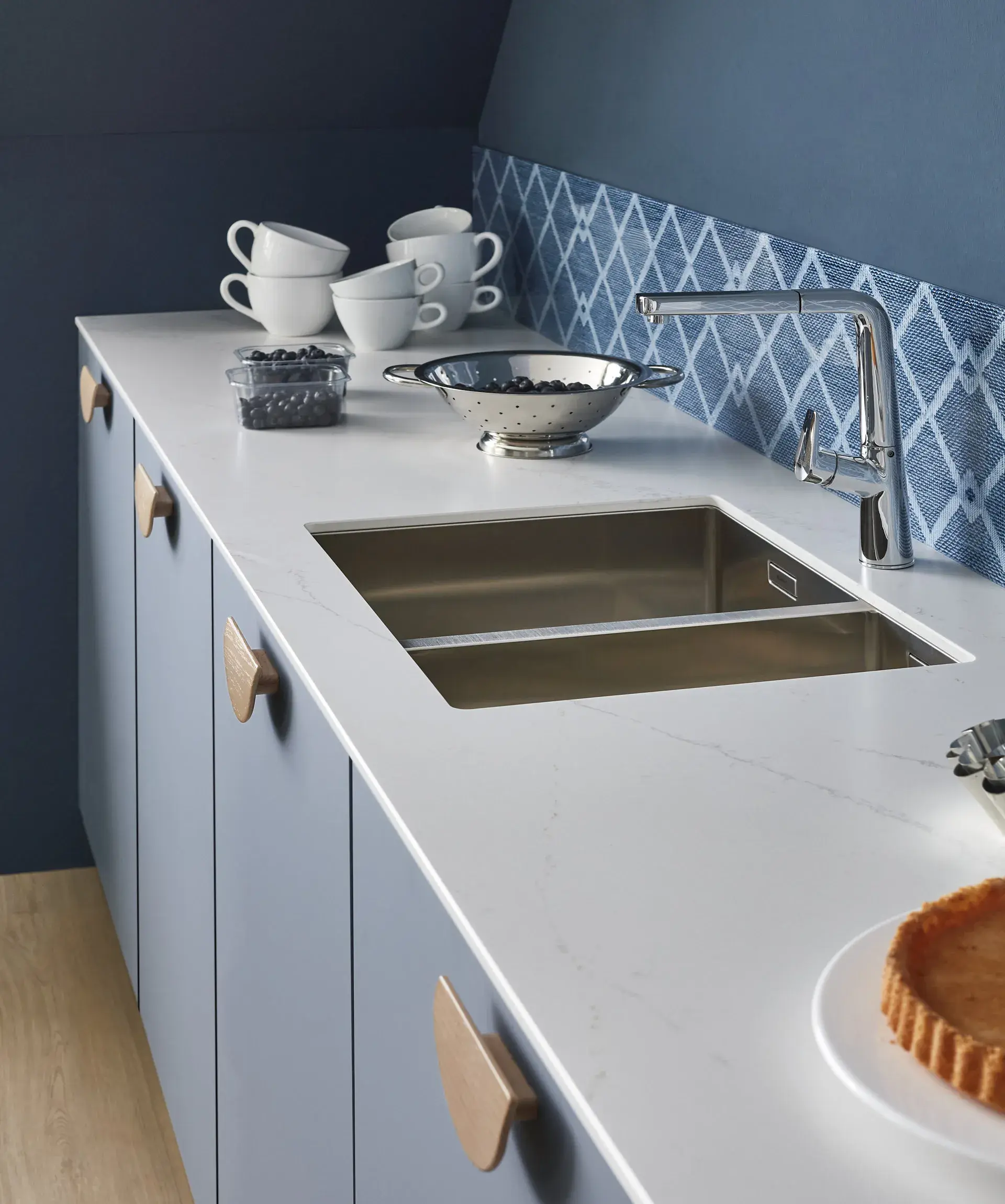 Küchenzeile mit Marmor-Arbeitsplatte pastellgraublaue Fronten Holzgriffe blau gemusterter Spritzschutz niedrig